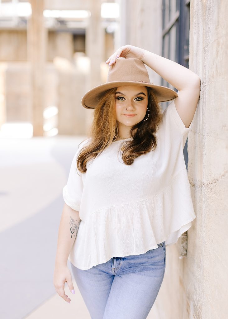 senior leans against wall with wide brimmed hat