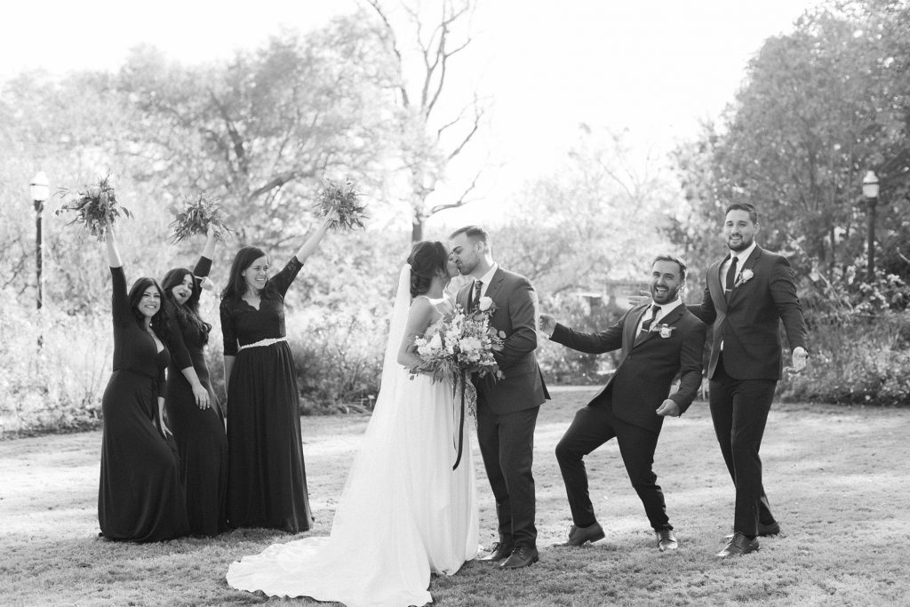 newlyweds kiss while bridal party cheers around them