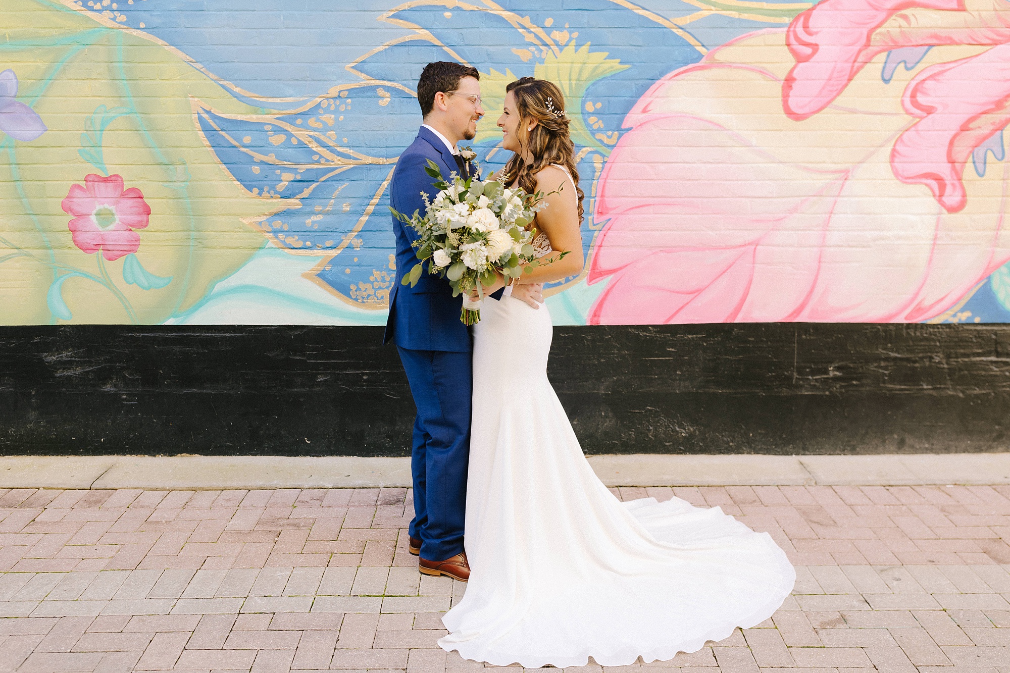 groom in navy suit holds bride by colorful mural in downtown Lakeland