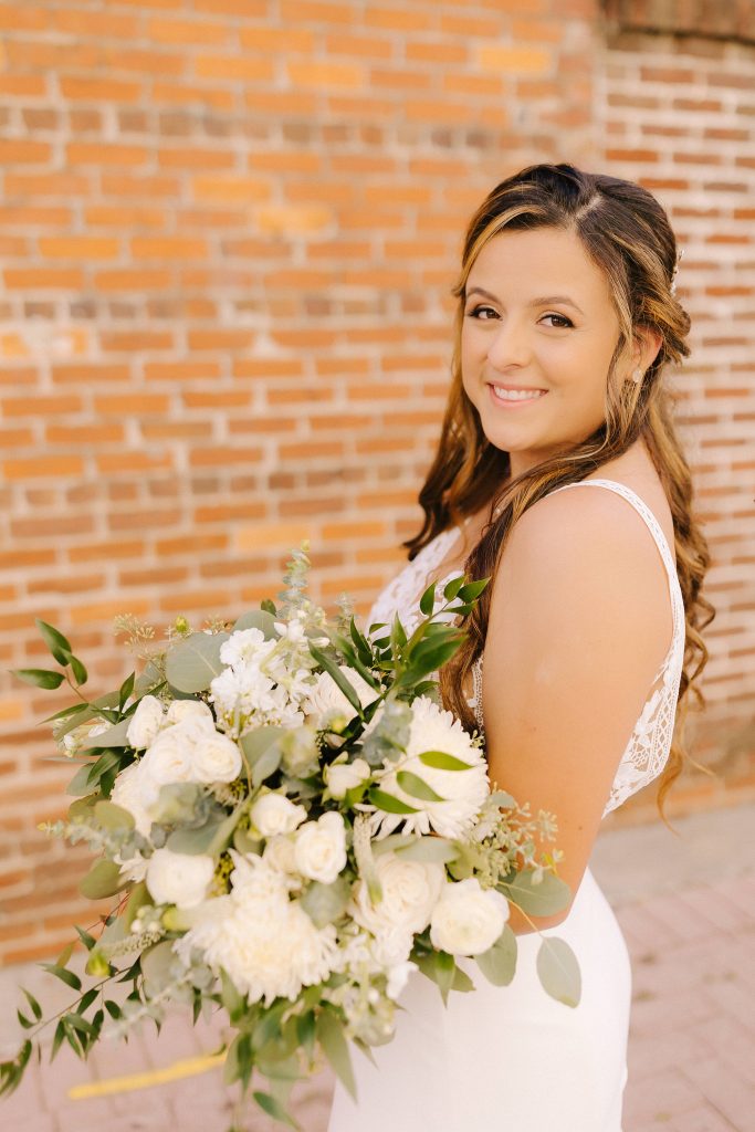bride holds bouquet of all white flowers in front of brick wall in Florida 