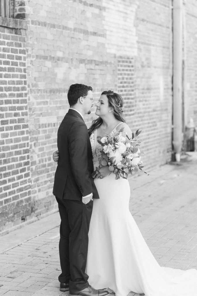 bride and groom kiss by brick wall 