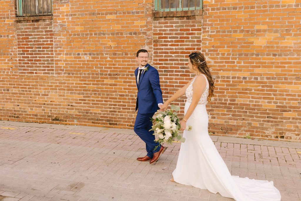 newlyweds walk by brick wall in downtown Lakeland