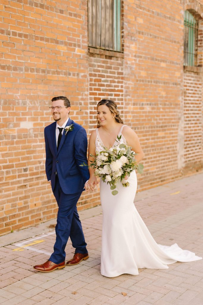 newlyweds walk in front of brick wall in downtown Lakeland