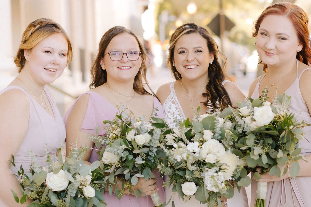 bride smiles with bridesmaids holding ivory bouquets and in pink gowns