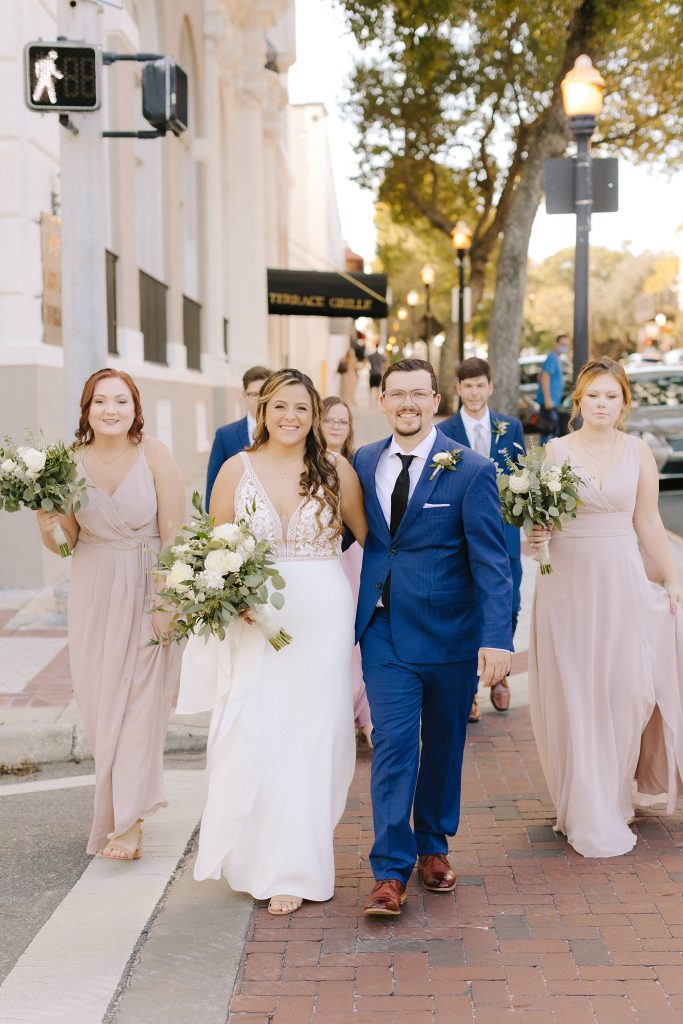 newlyweds walk down street with bridal party