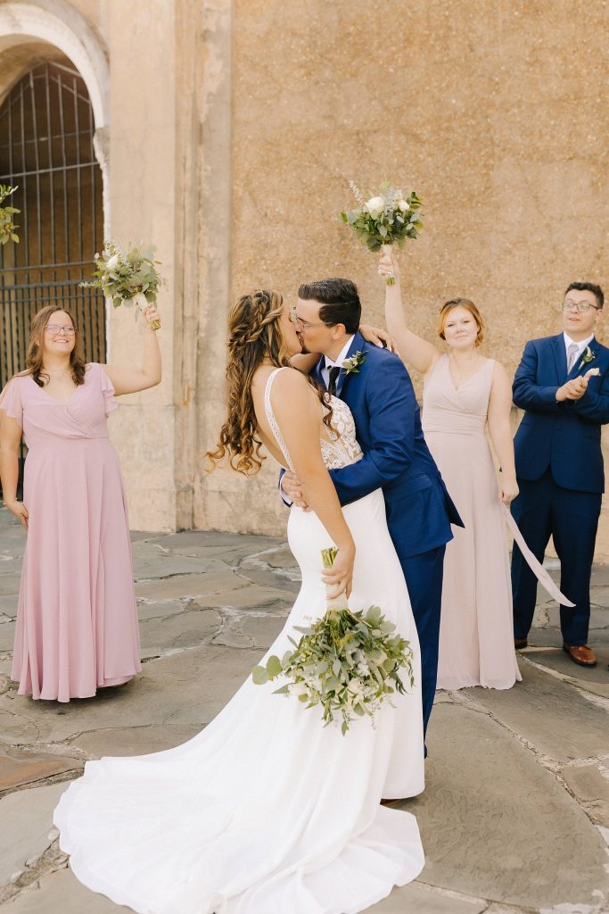 groom kisses bride with bridal party cheering