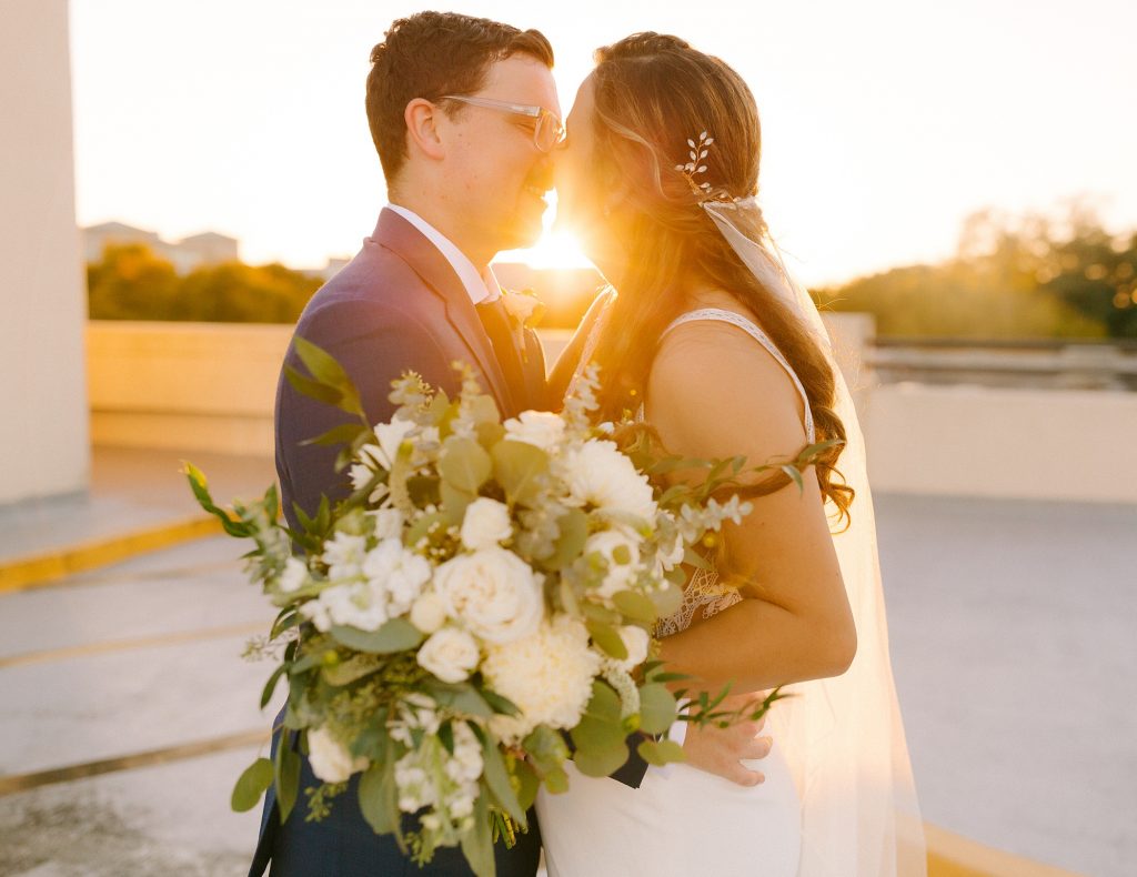bride and groom stand nose to nose with sunset around them