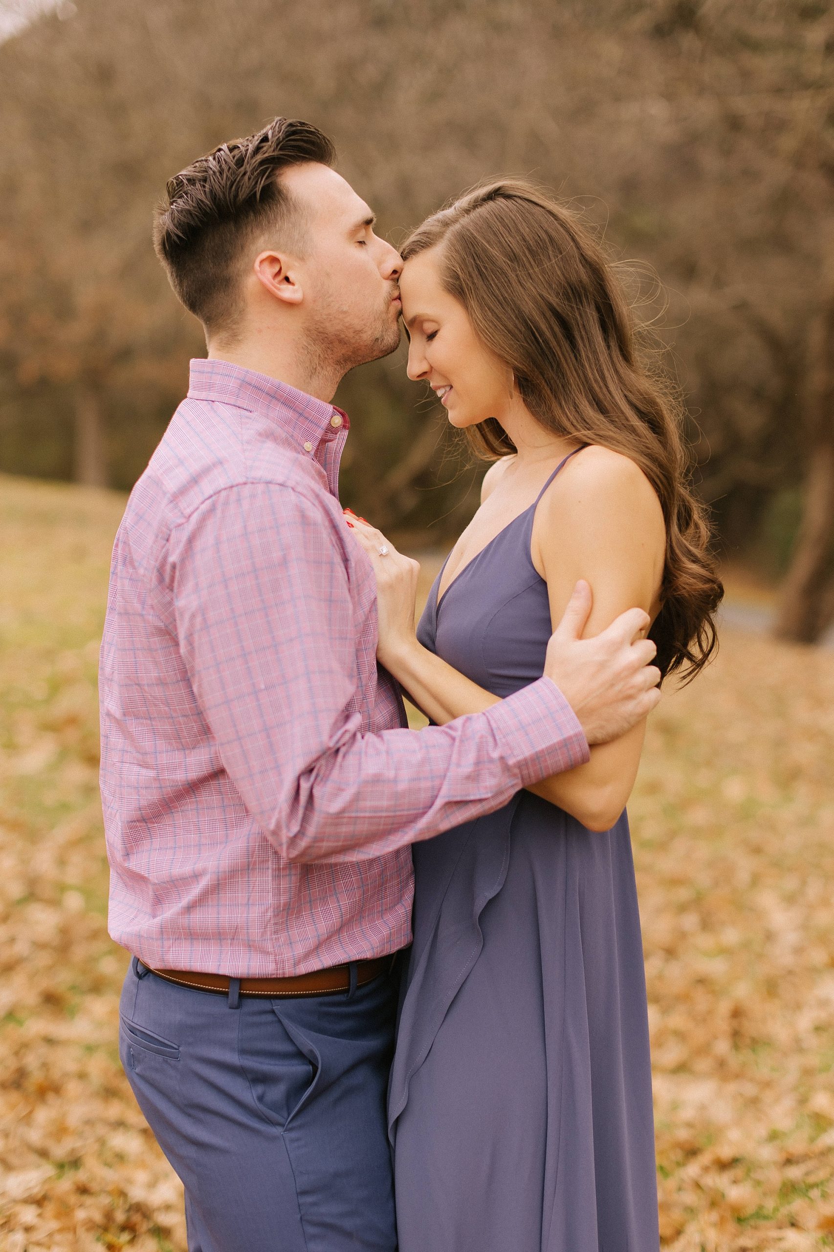 groom kisses fiancee's forehead during fall engagement photos 