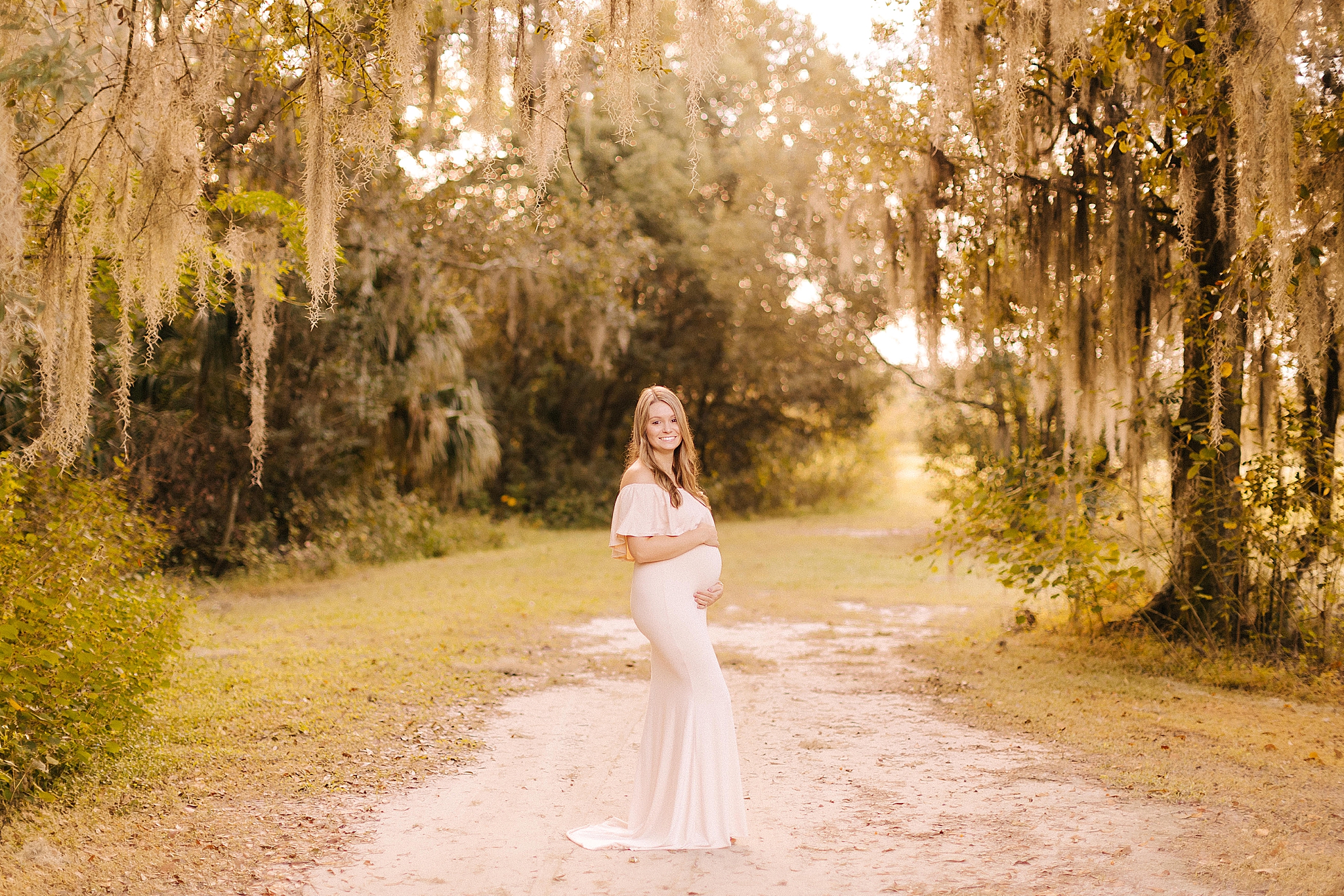 mom stands in between spanish moss during maternity session
