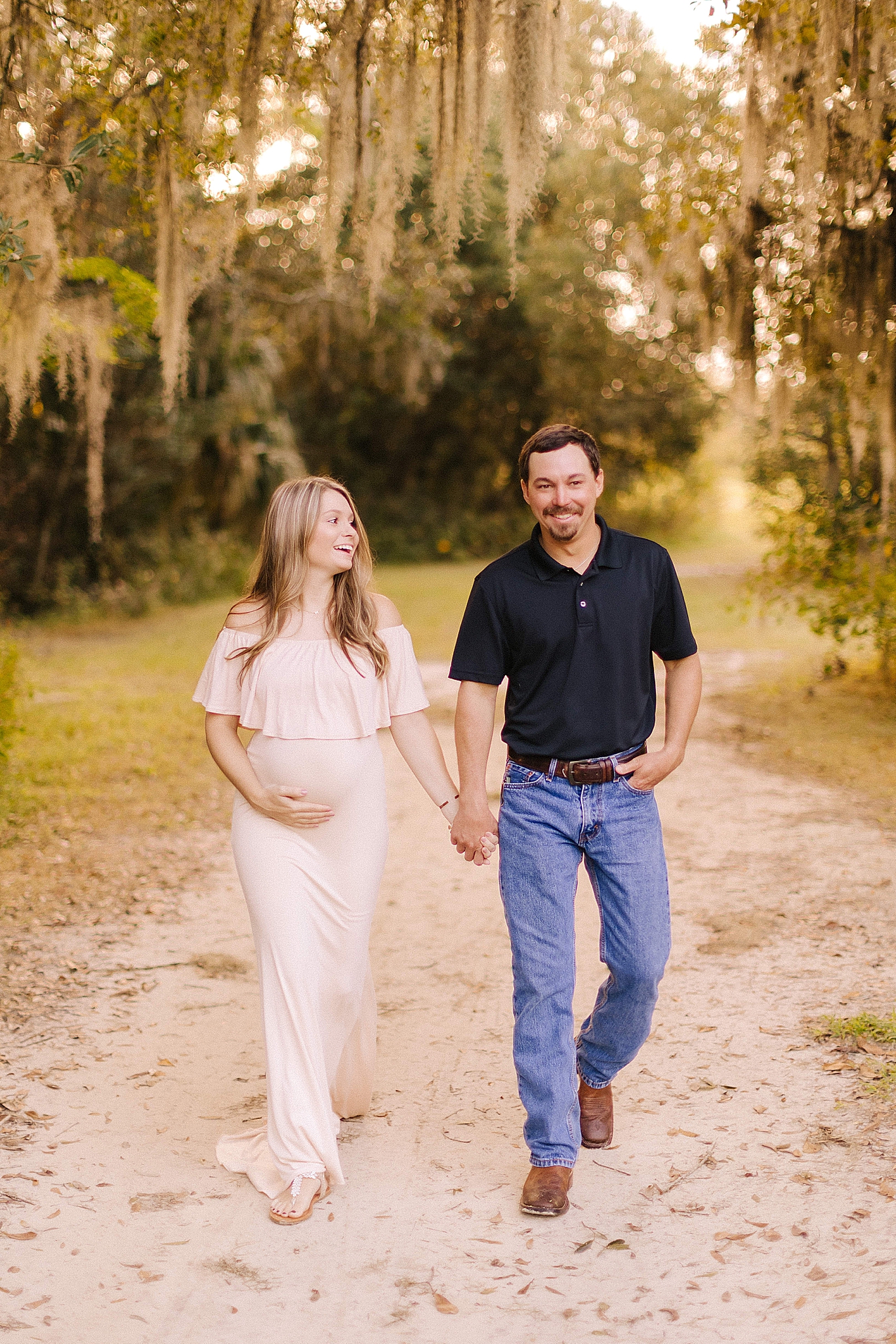 mom and dad hold hands walking down dirt path during Winston Salem maternity photos