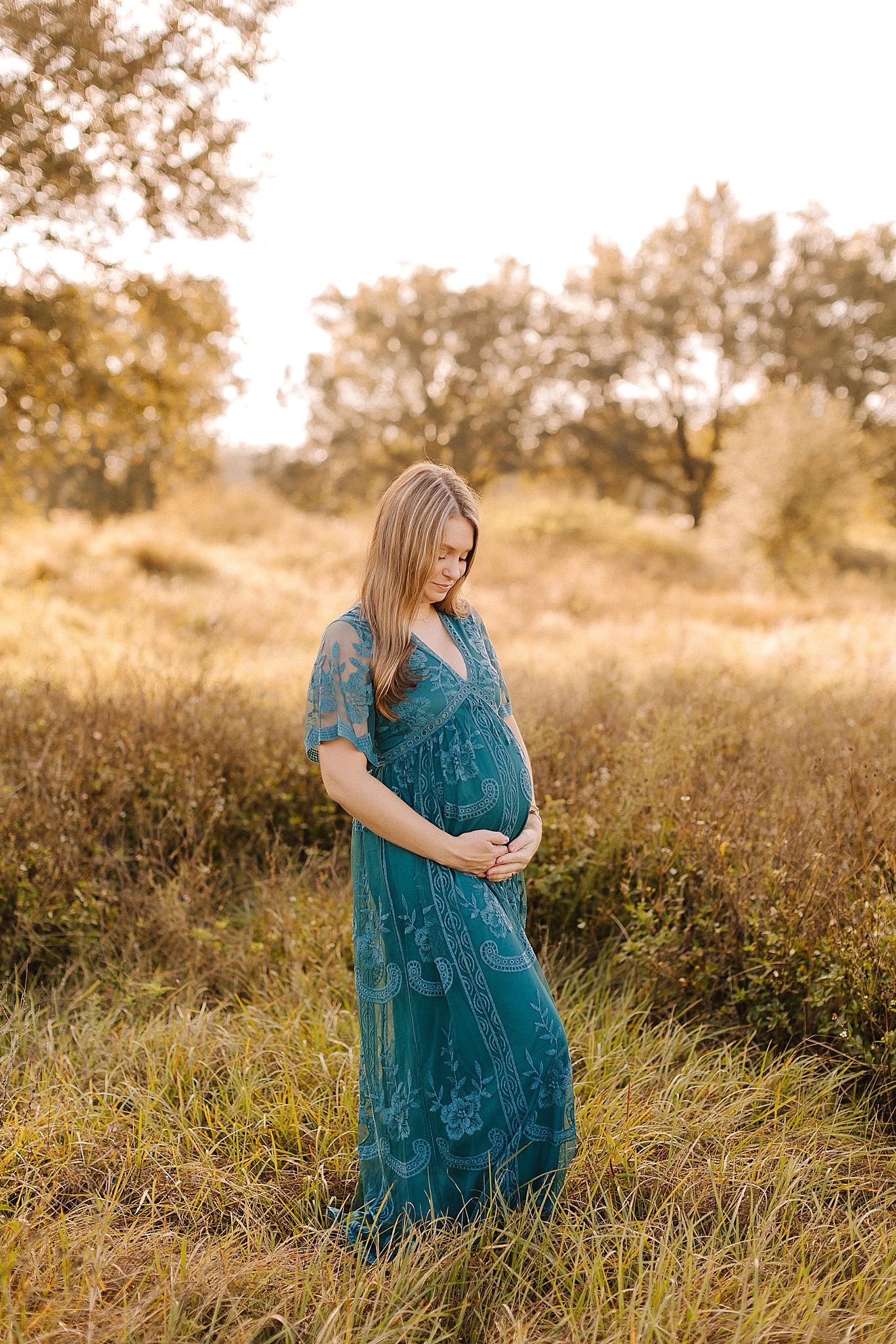 mom holds belly in teal maternity gown Winston Salem maternity photos