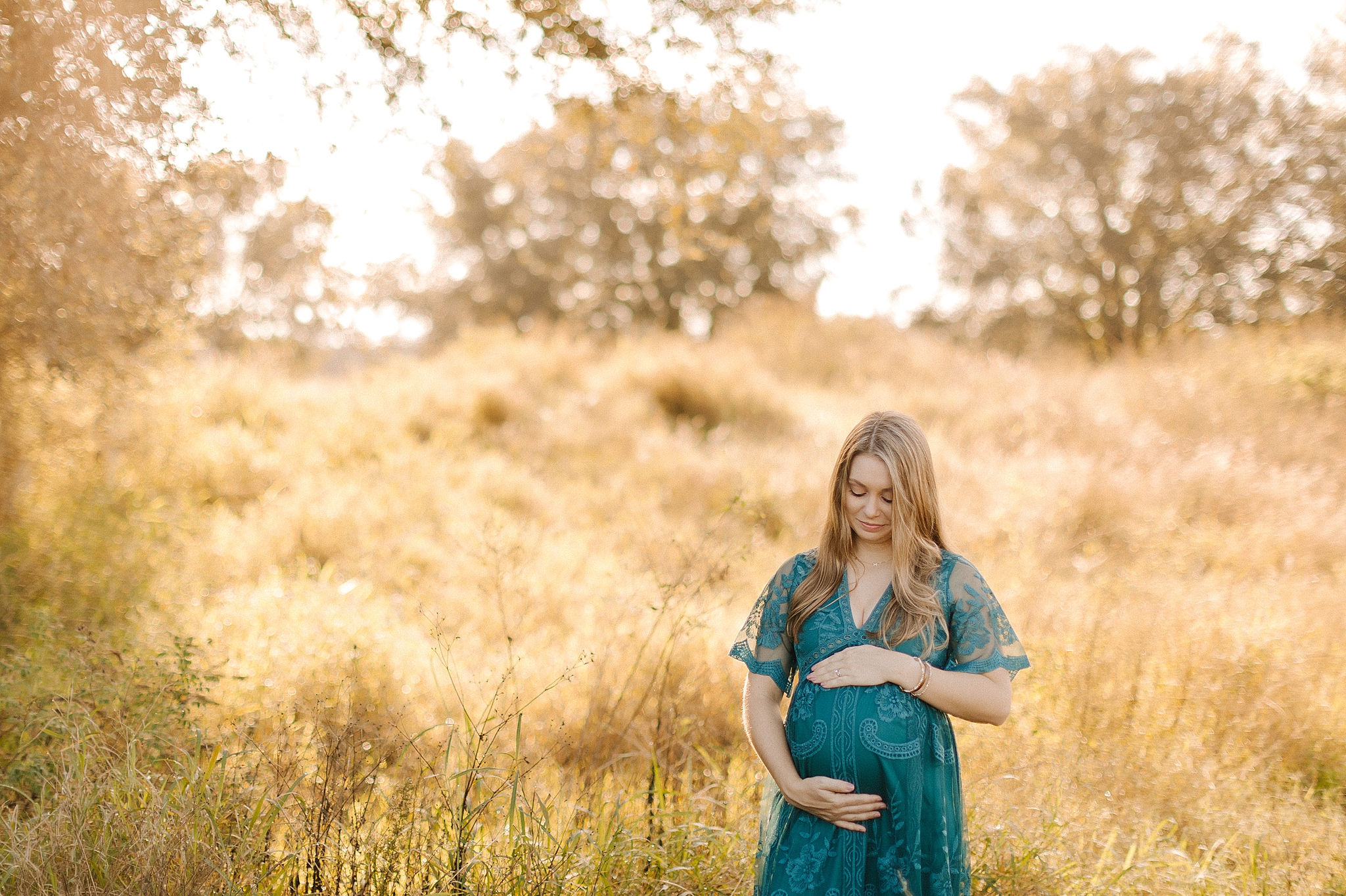 mom in boho teal maternity gown holds belly during maternity photos