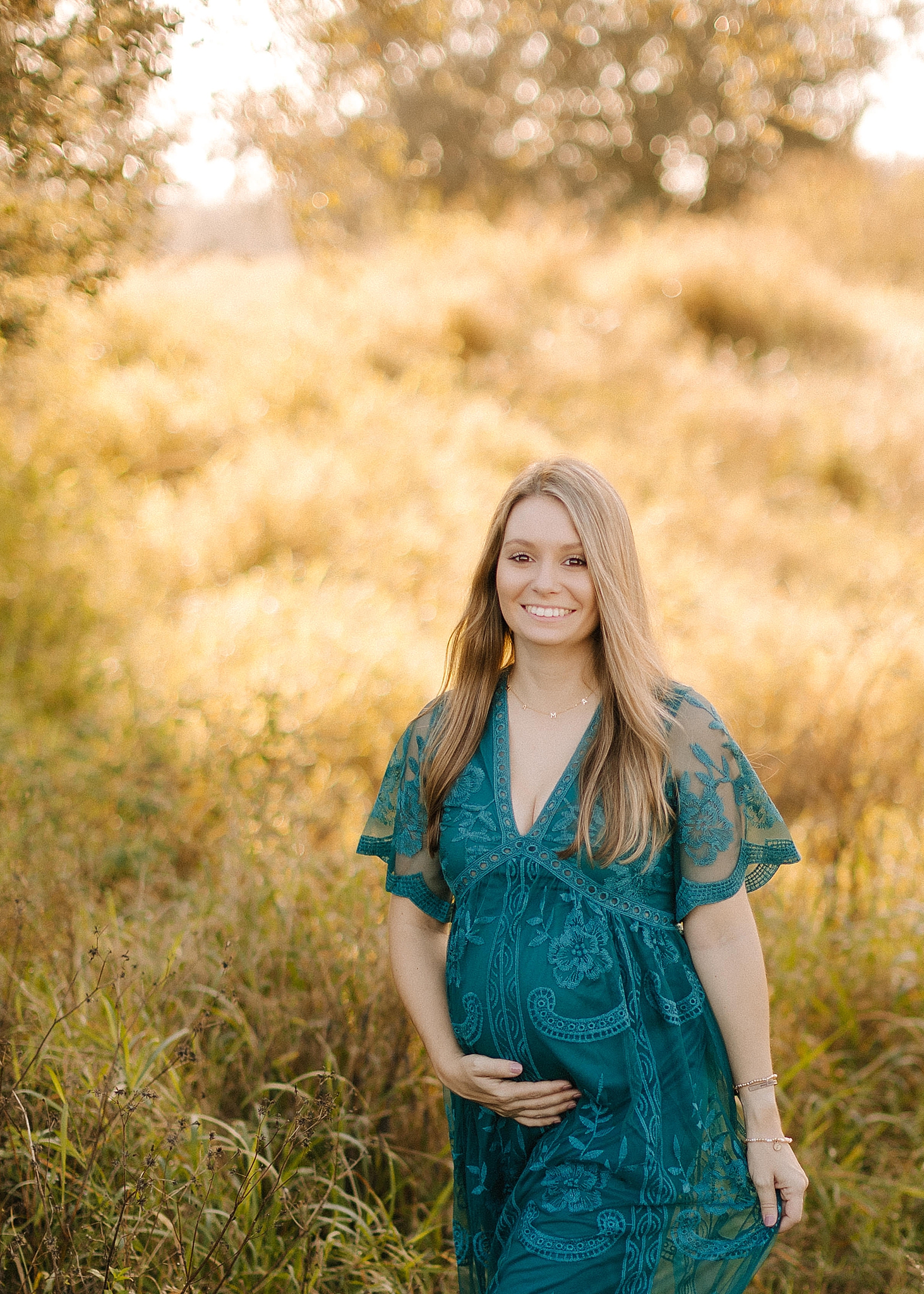mom smiles holding round belly during maternity photos in teal gown