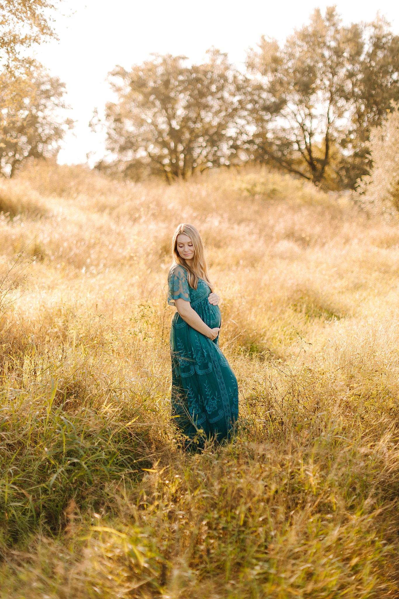 mother stands in field wearing teal boho maternity gown during Winston Salem maternity photos