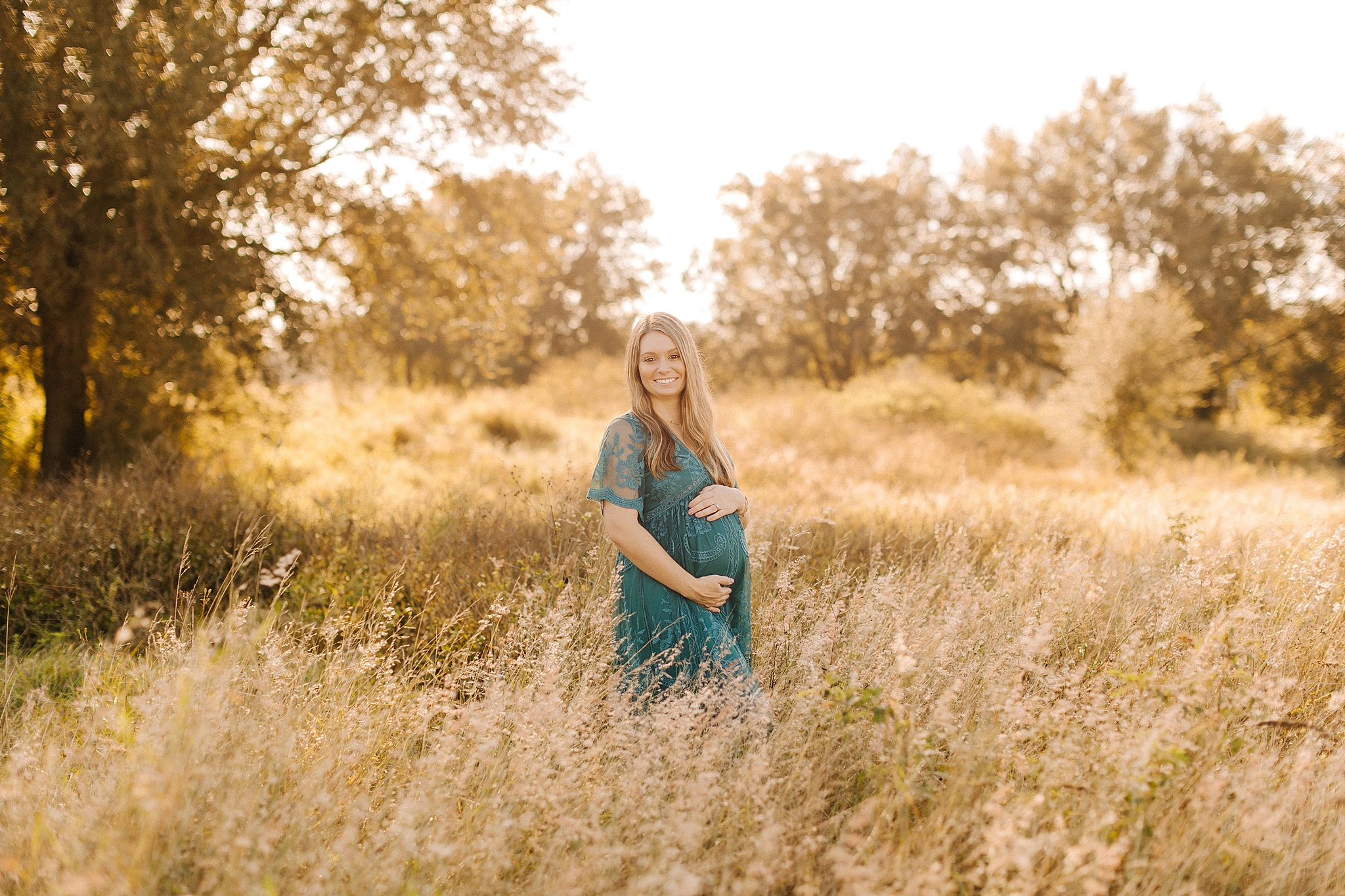 mom in teal boho maternity gown poses in field