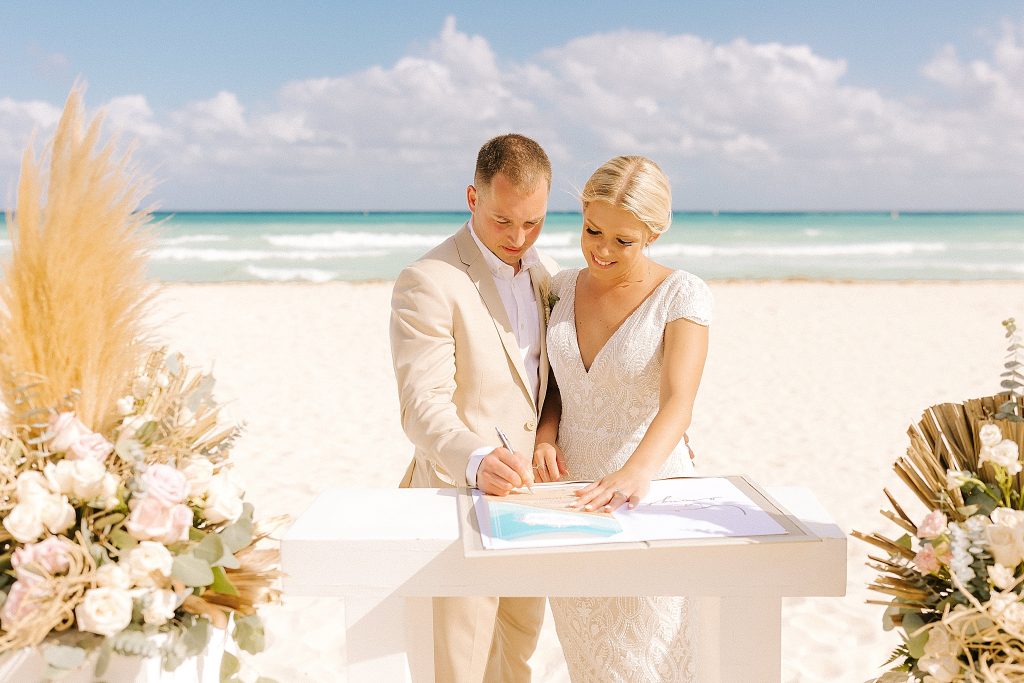 bride and groom sign wedding license during destination wedding ceremony on the beach in Playa Del Carmen
