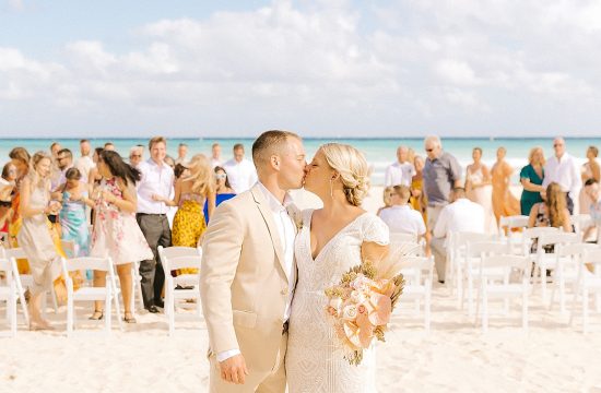 newlyweds kiss with guests behind them after destination wedding ceremony on the beach in Playa Del Carmen