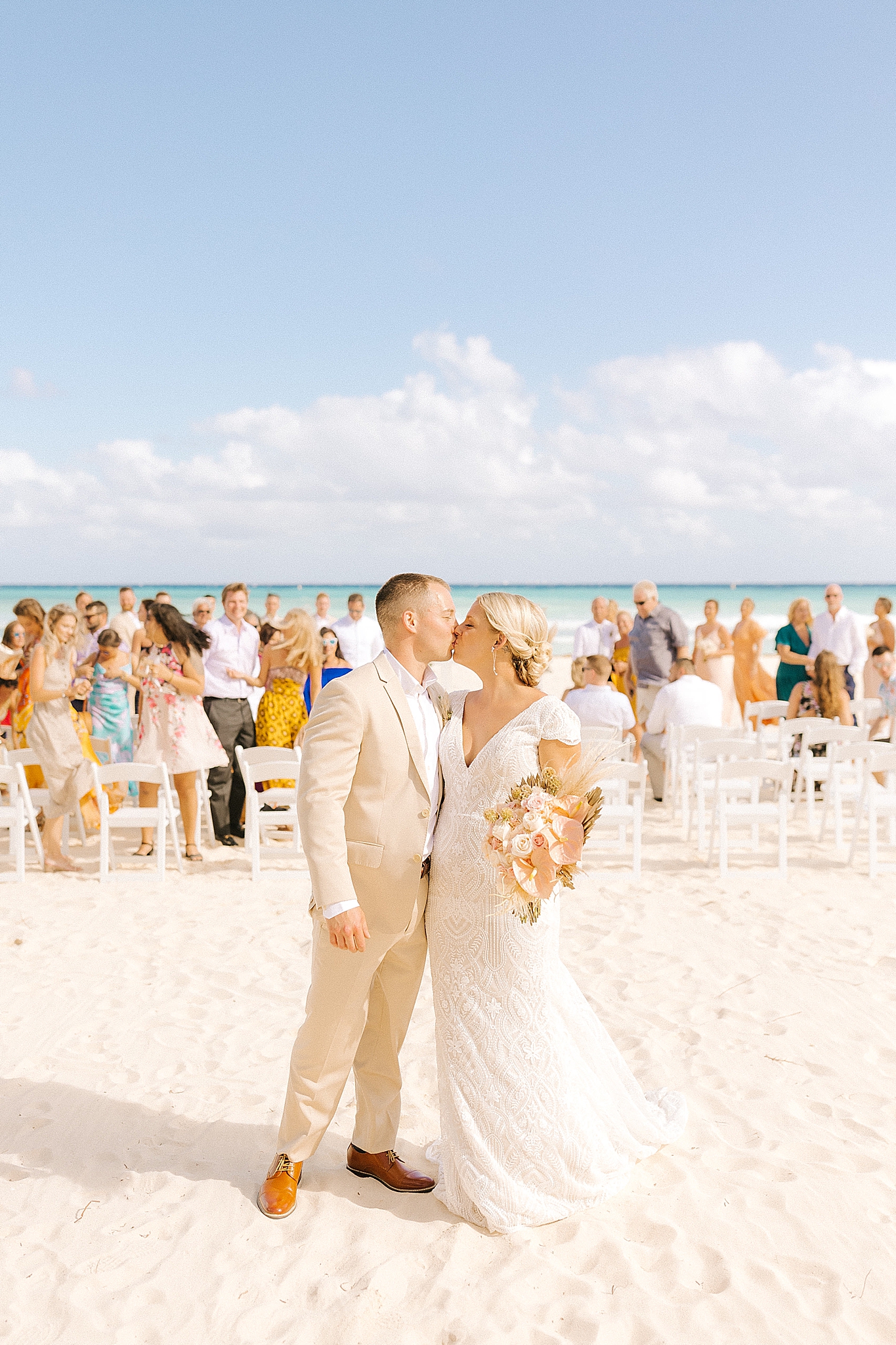 newlyweds kiss with guests behind them after destination wedding ceremony on the beach in Playa Del Carmen