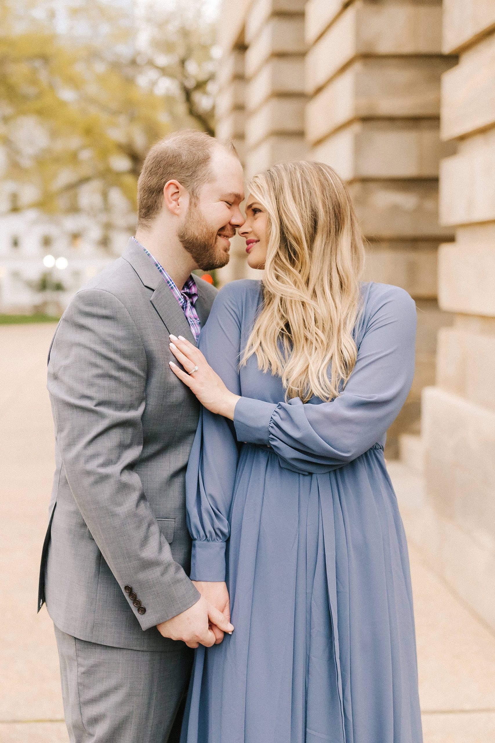 bride leans against groom's chest during fall Downtown Raleigh engagement photos 
