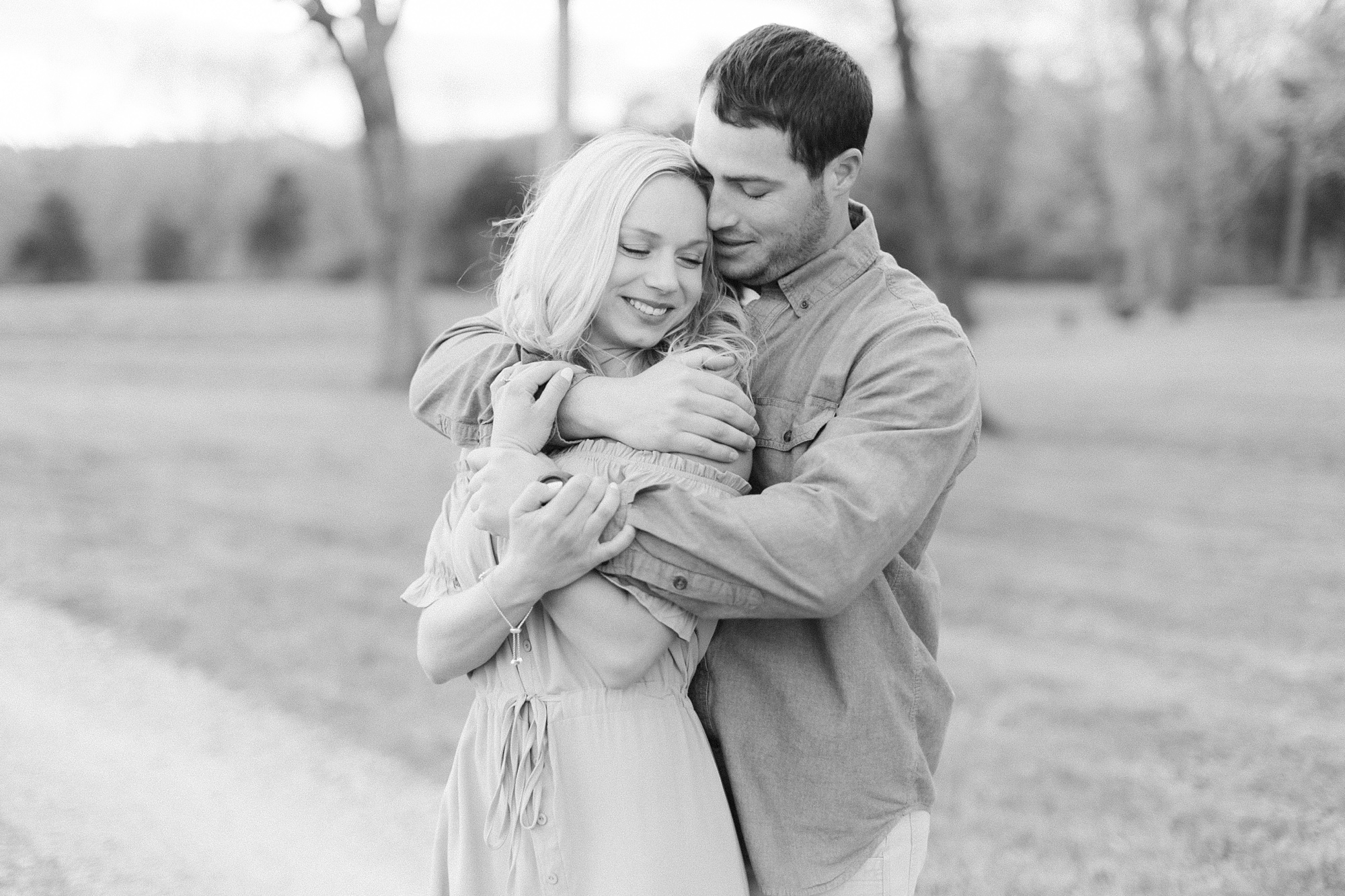 groom hugs fiancee from behind during Summerfield Farms engagement session