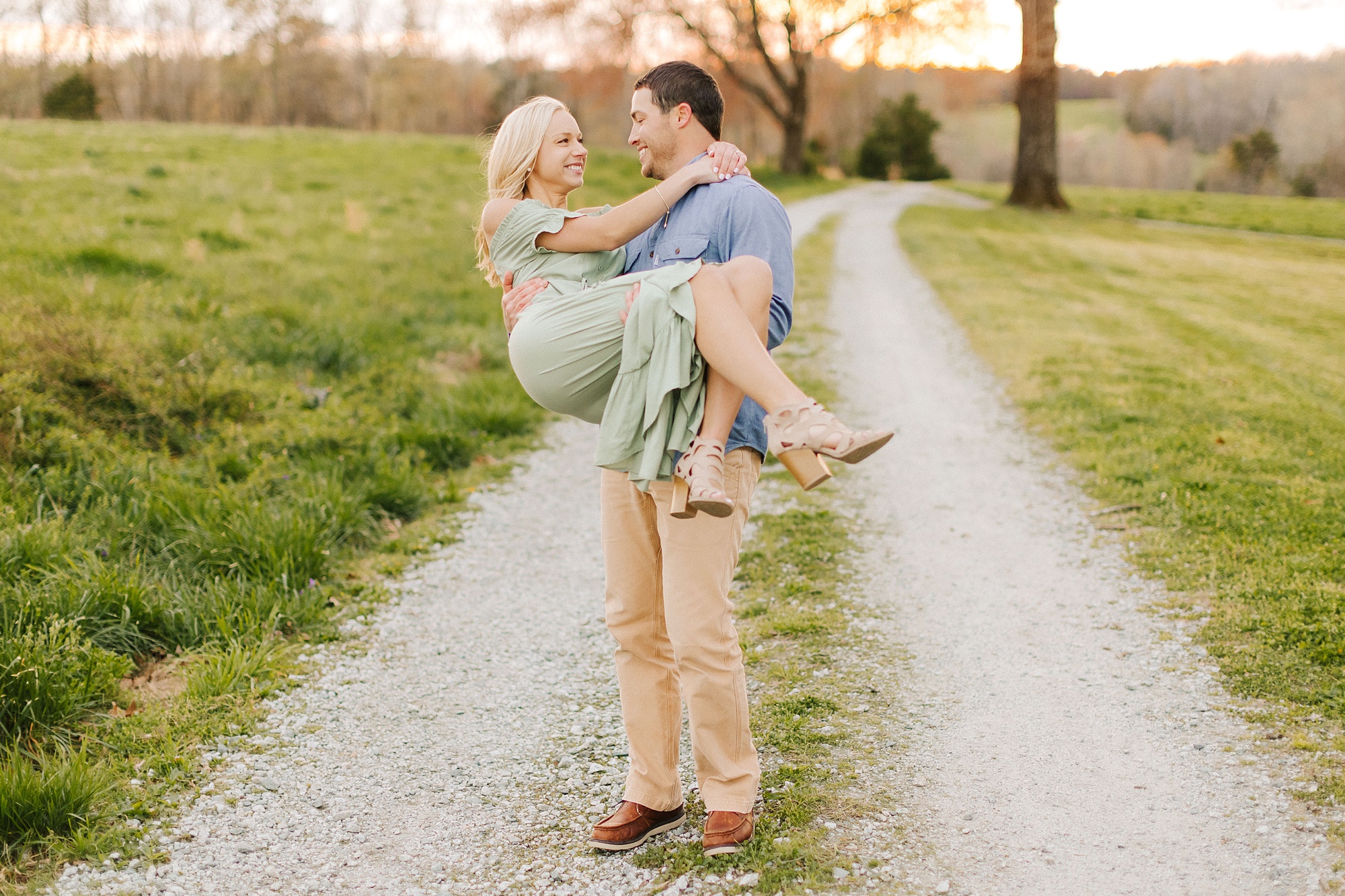 groom lifts fiancee standing on path during Summerfield Farms engagement photos
