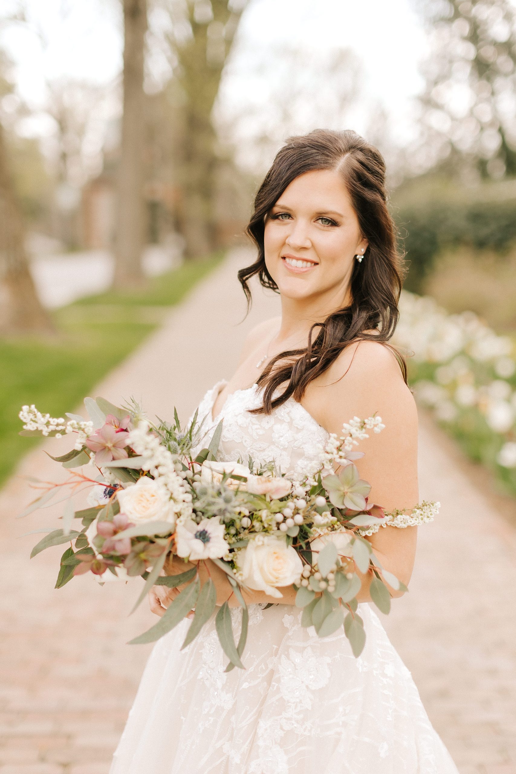 bride poses in gardens holding bouquet of muted flowers 