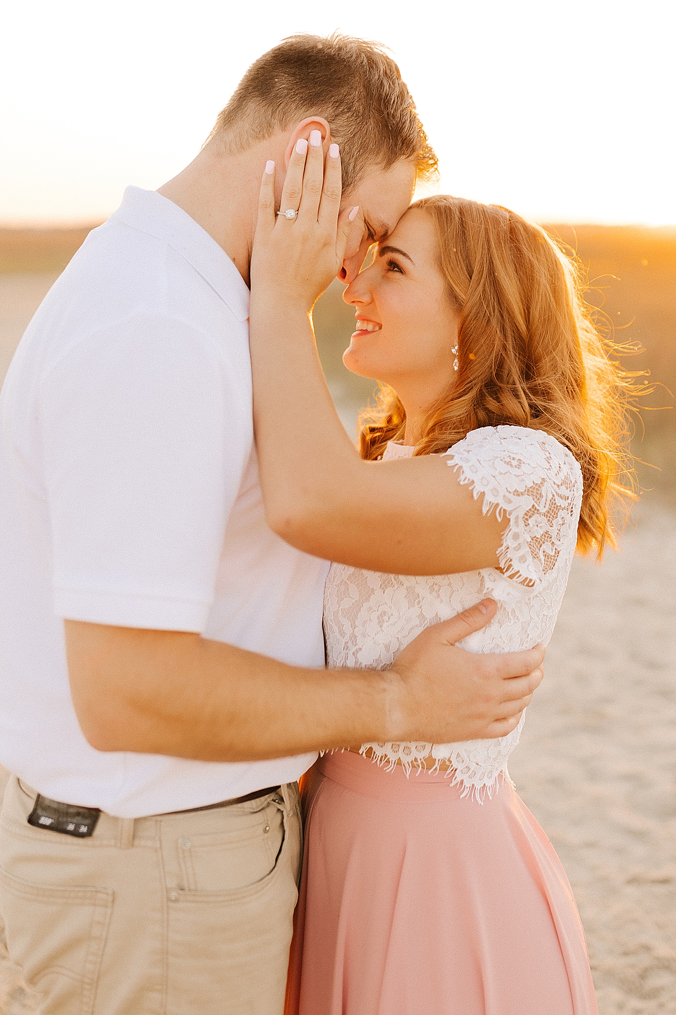 bride holds groom's head showing off engagement ring on beach