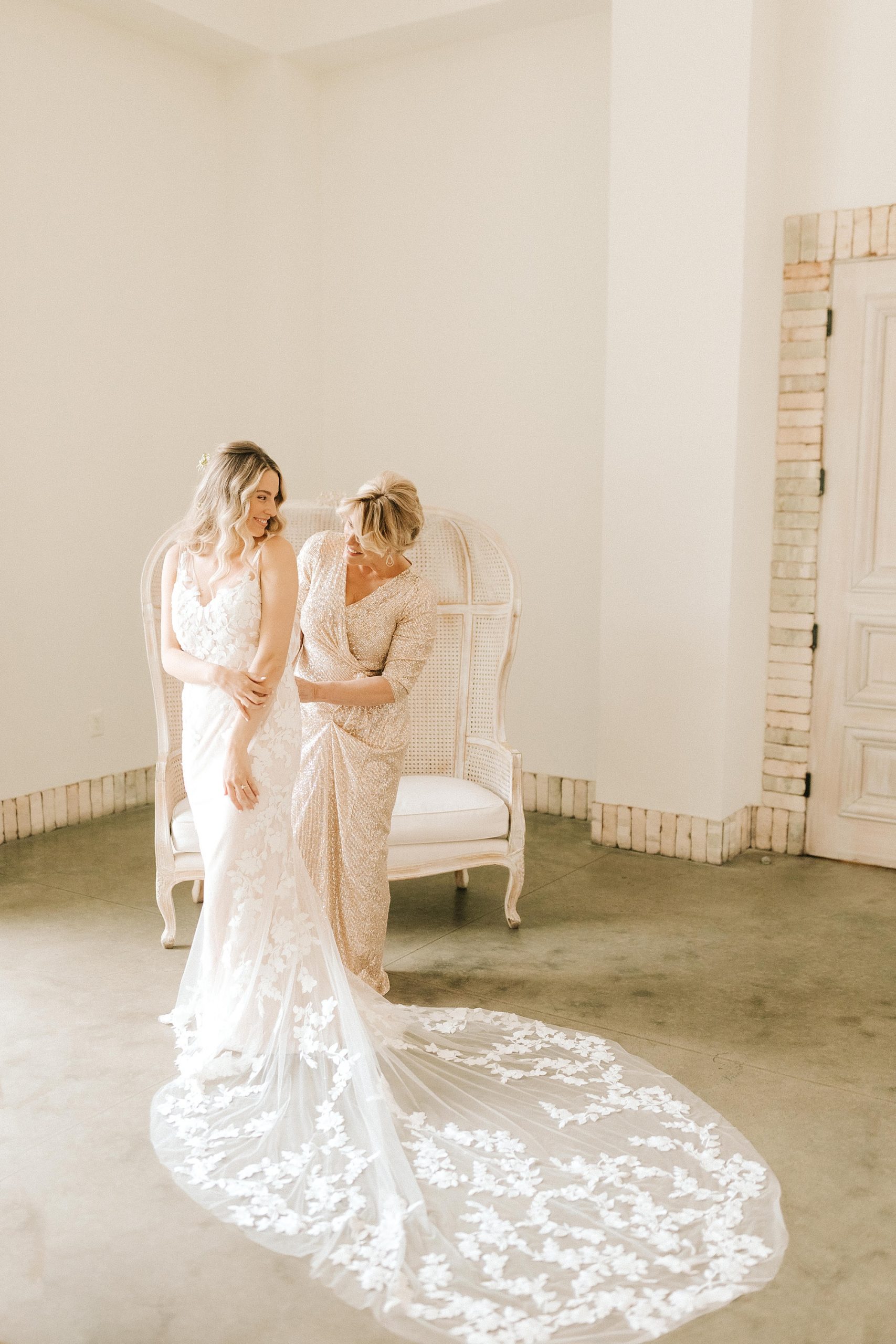 mother of the bride helps bride with wedding dress