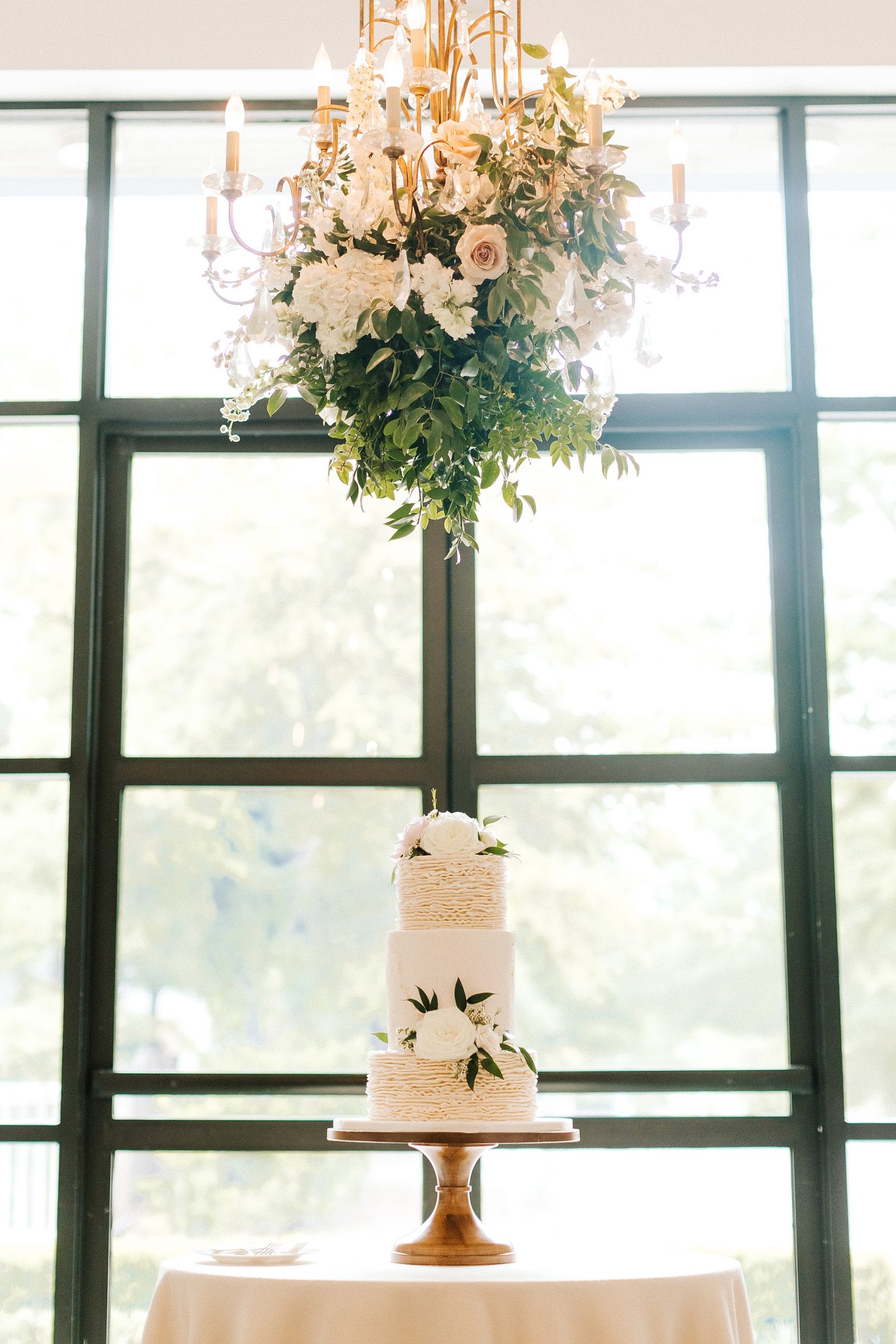 wedding cake sits under hanging floral arrangement at Wrightsville Manor