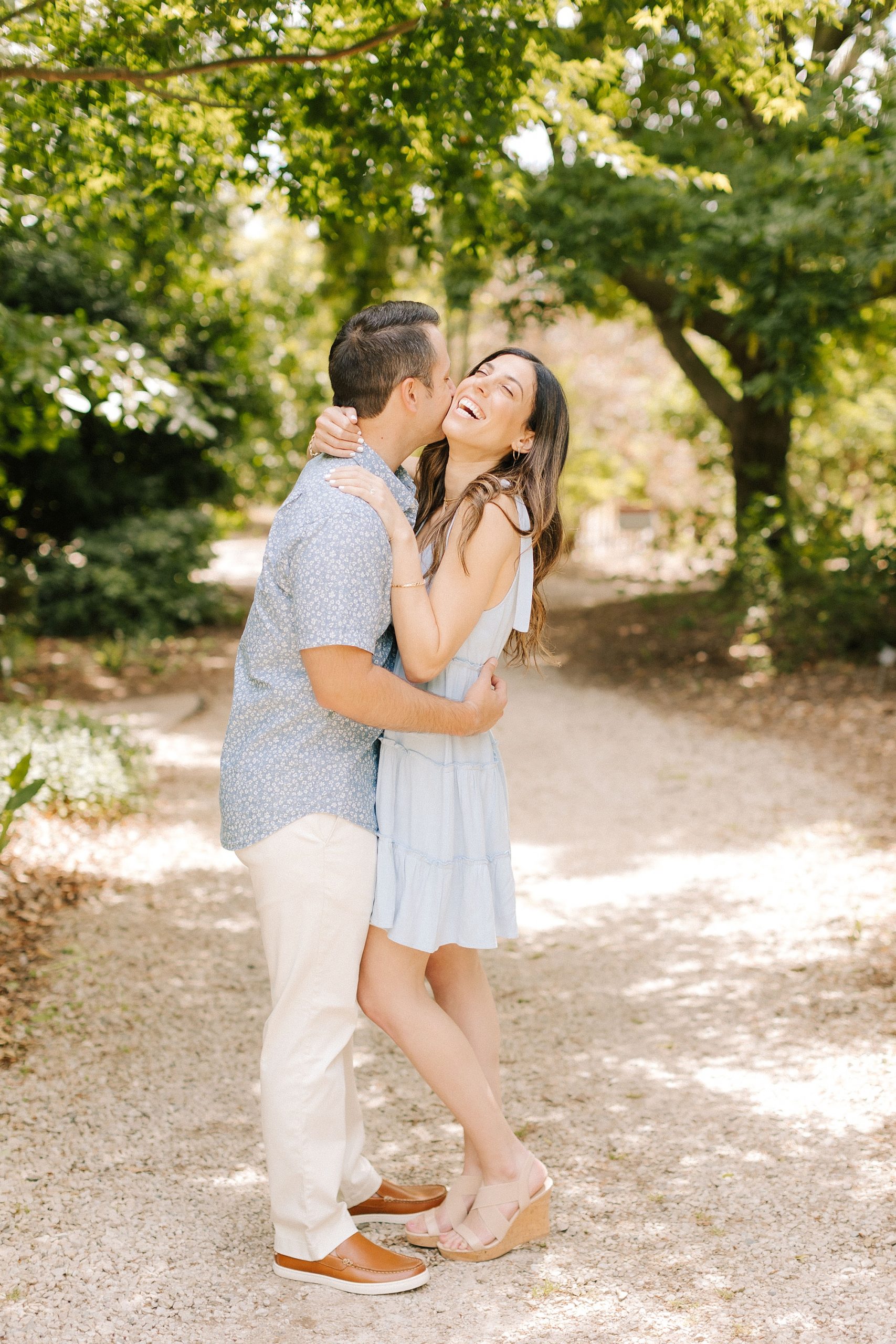 groom kisses bride's cheek making her laugh during Raleigh NC engagement session