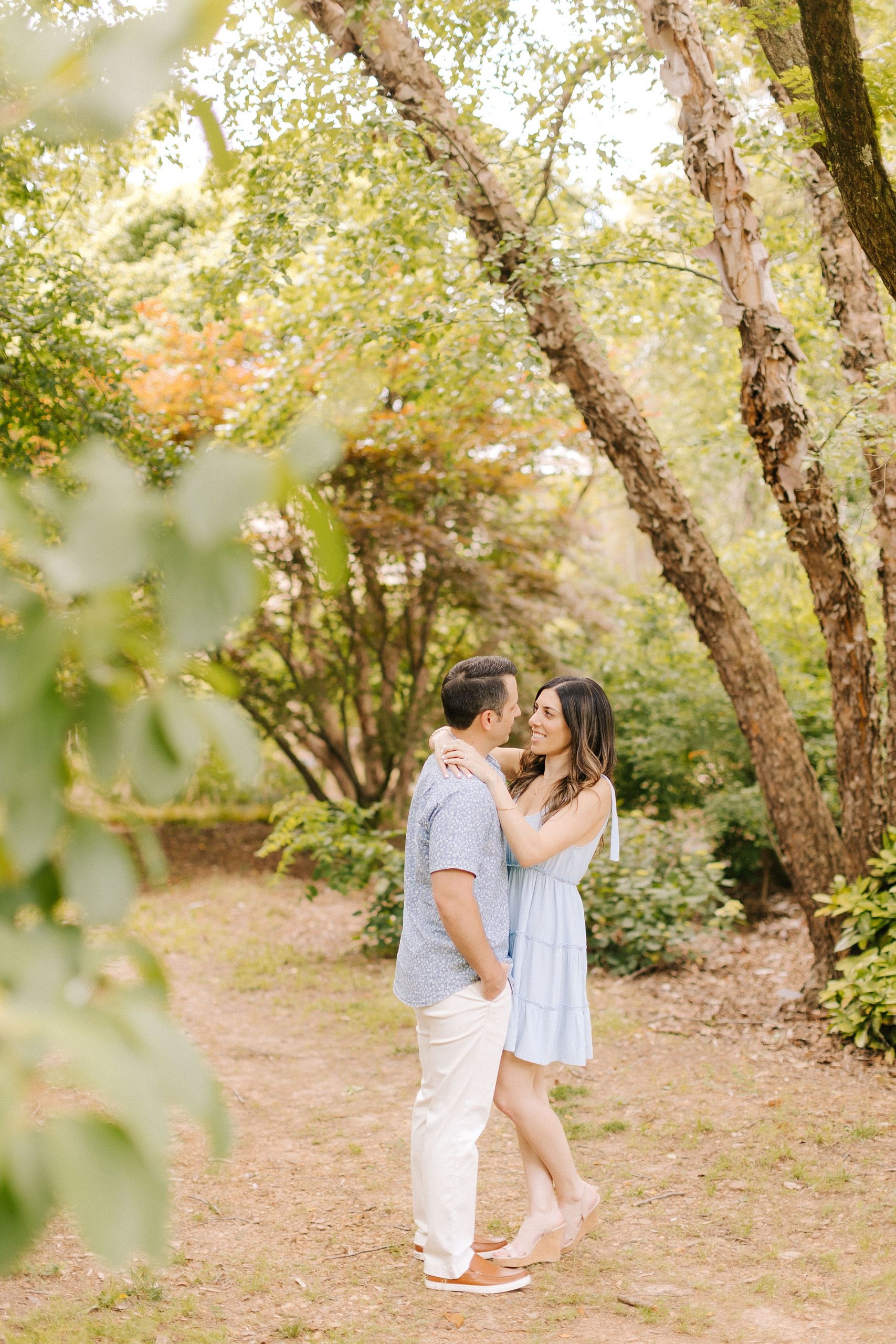 engaged couple hugs in clearing at JC Raulston Arboretum