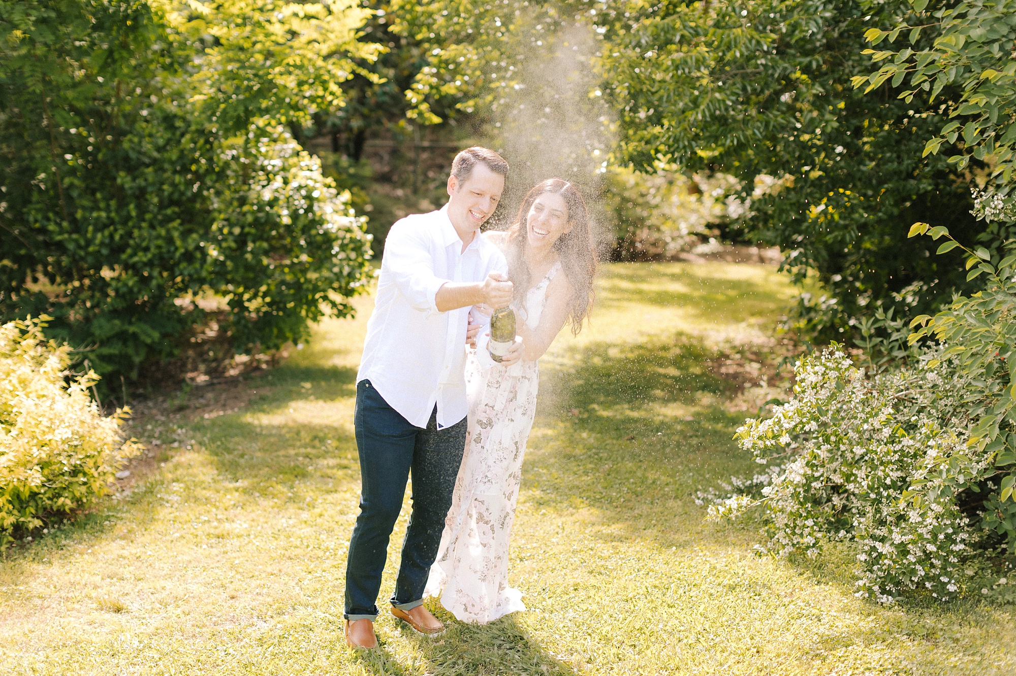 couple pops bottle of champagne during engagement photos in Raleigh NC
