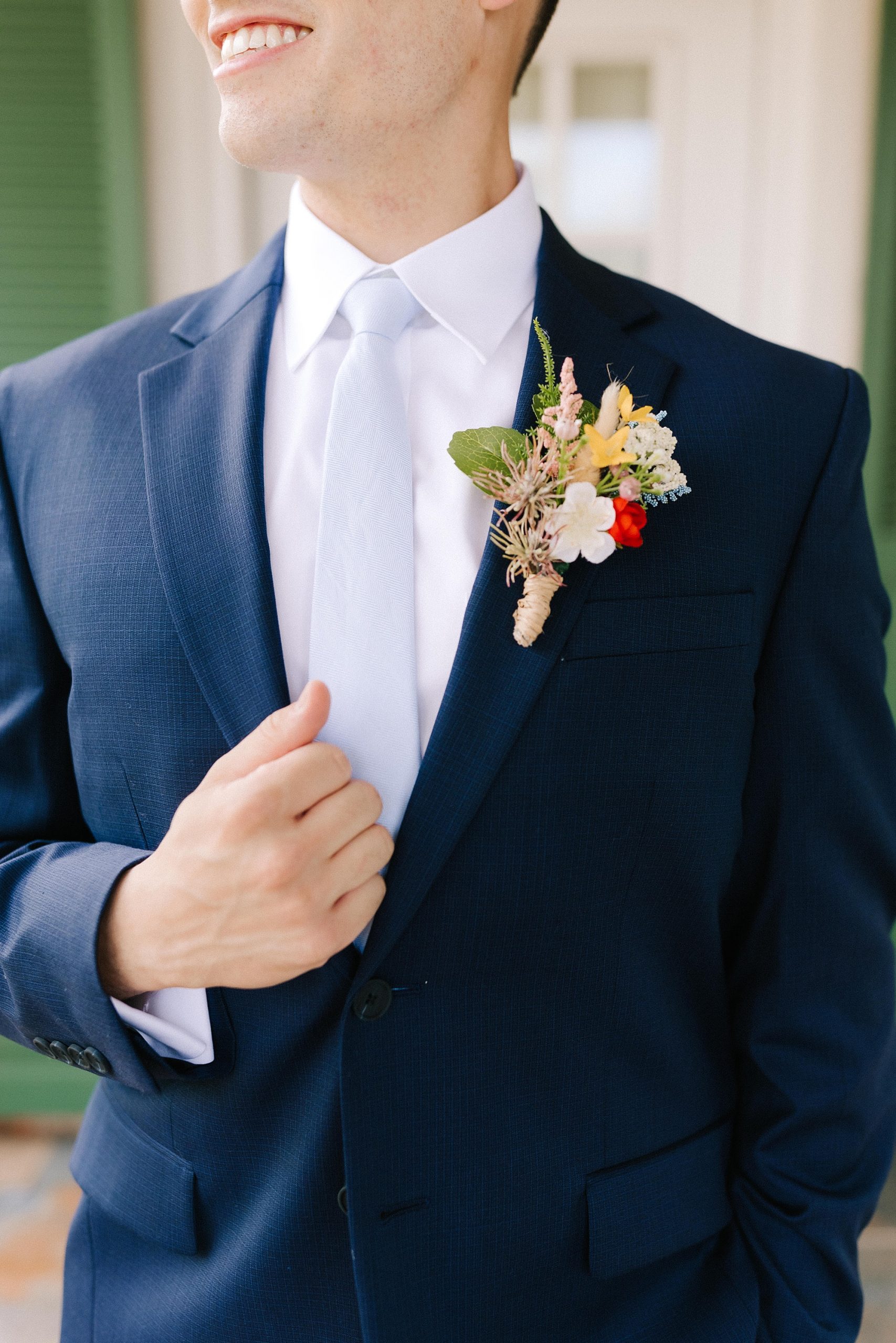 groom holds lapel of navy suit outside Moore's Spring Manor