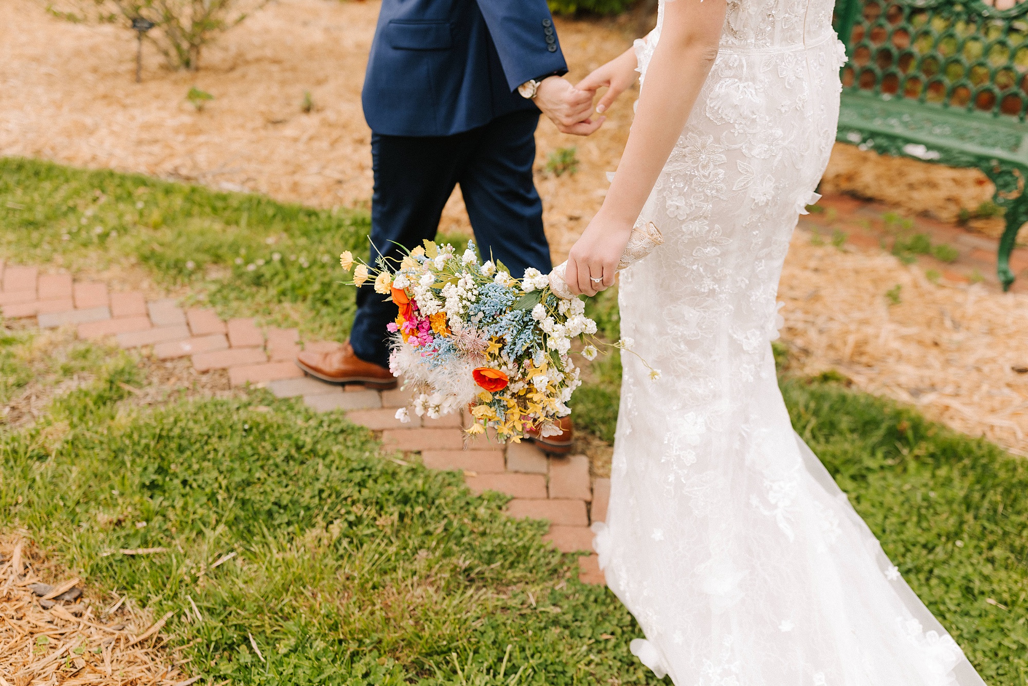 bride and groom hold hands walking through field