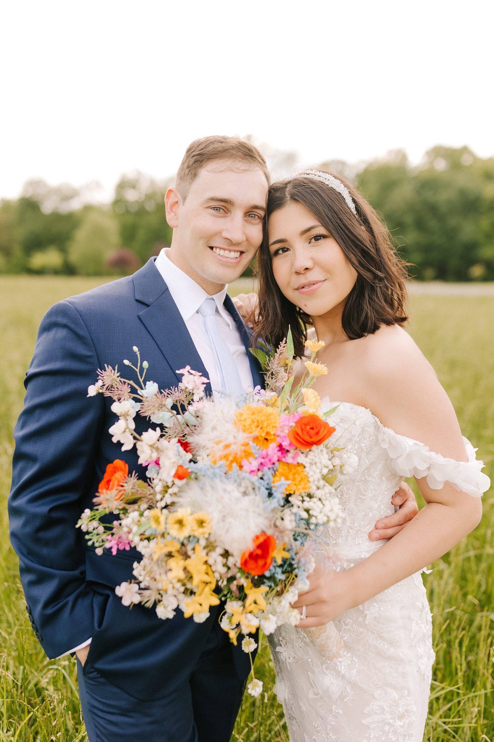 newlyweds stand together in field with bride holding bouquet of bright wildflowers 