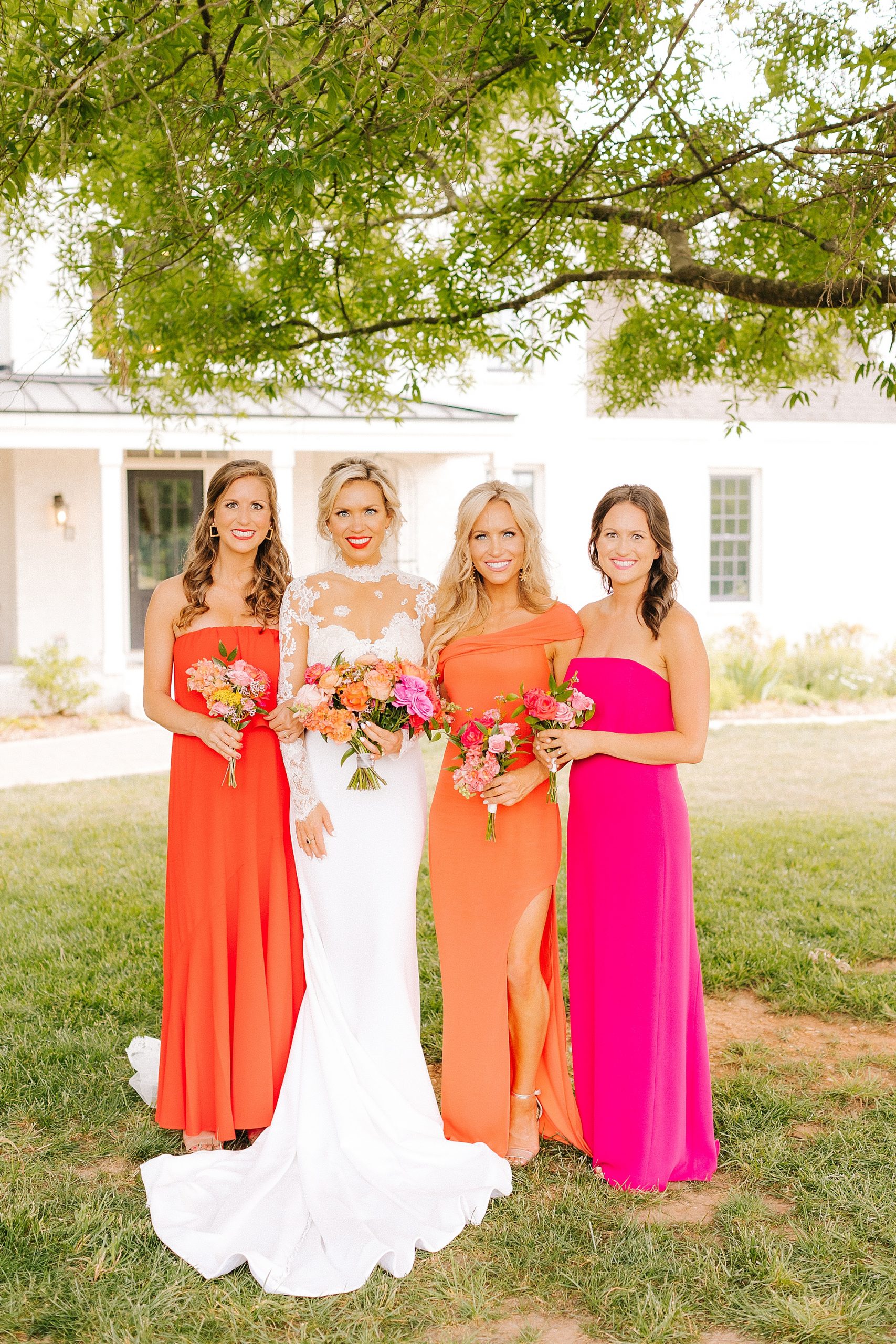 bride poses with bridesmaids in bright orange and pink gowns