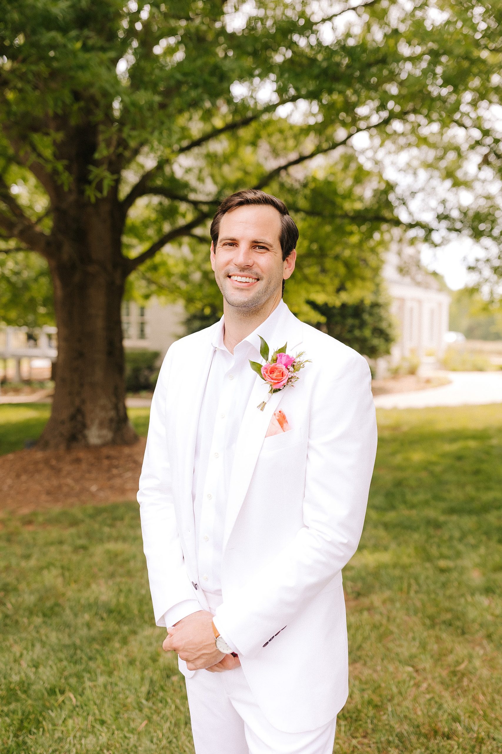 groom in white suit jacket smiles with colorful flower boutonnière 