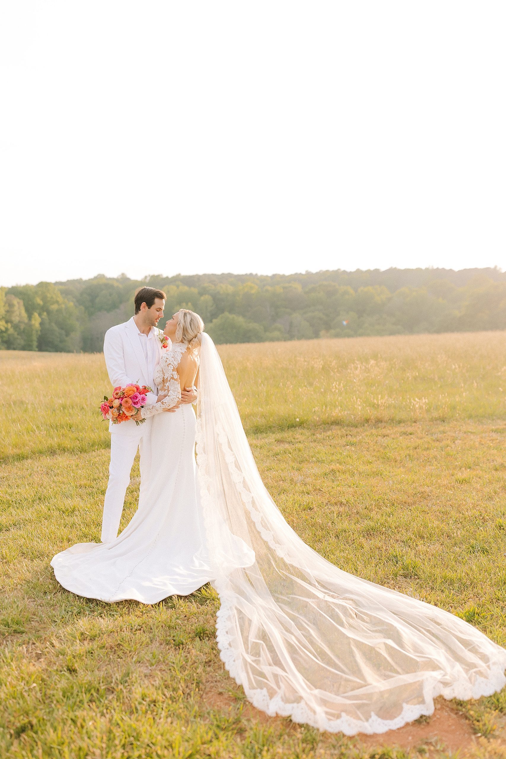 newlyweds stand together in field at sunset at The Meadows Raleigh