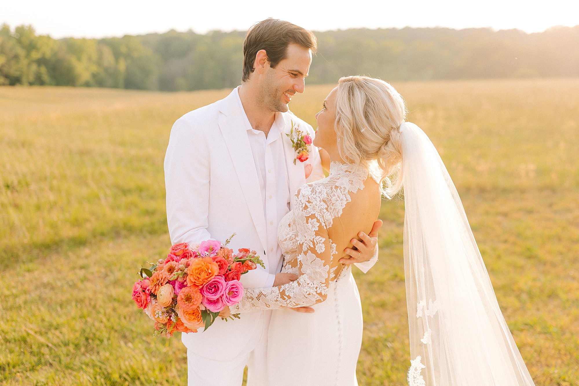 bride and groom hug while holding bouquet of pink and orange flowers 