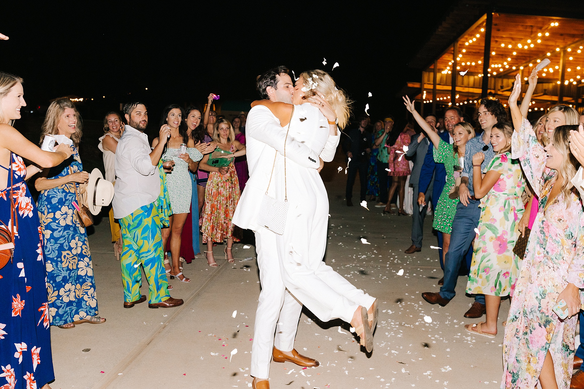 groom lifts bride in white pantsuit during exit