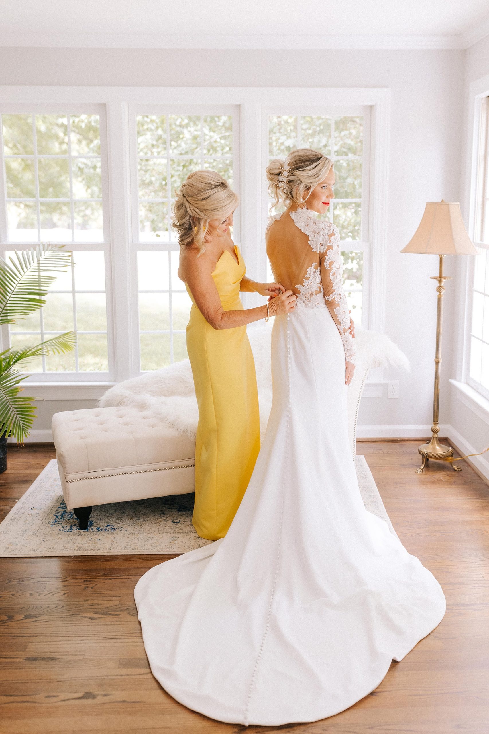 mother of the bride in yellow dress helps bride with wedding gown