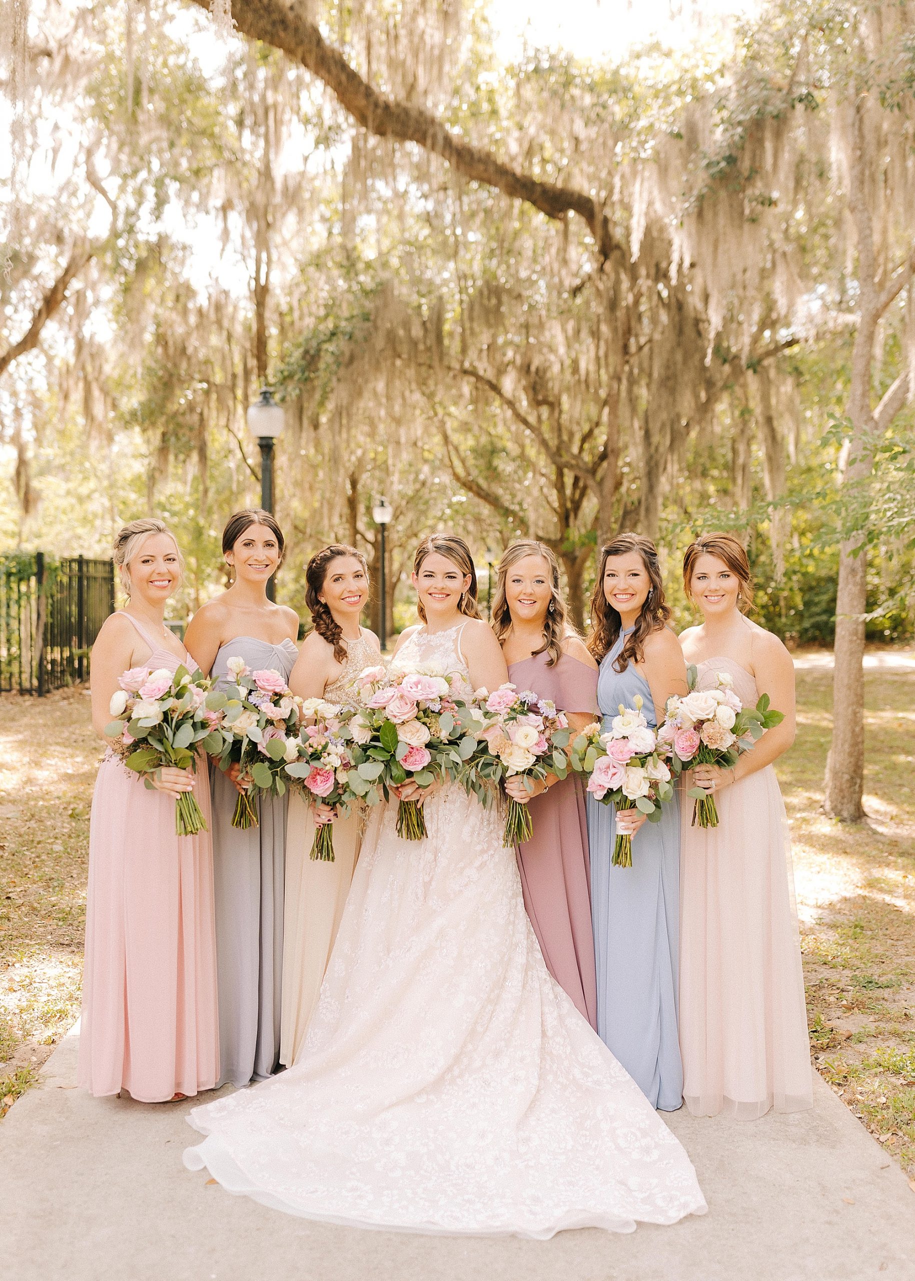 bride and bridesmaids in mismatched pastel gowns pose in Gainesville FL