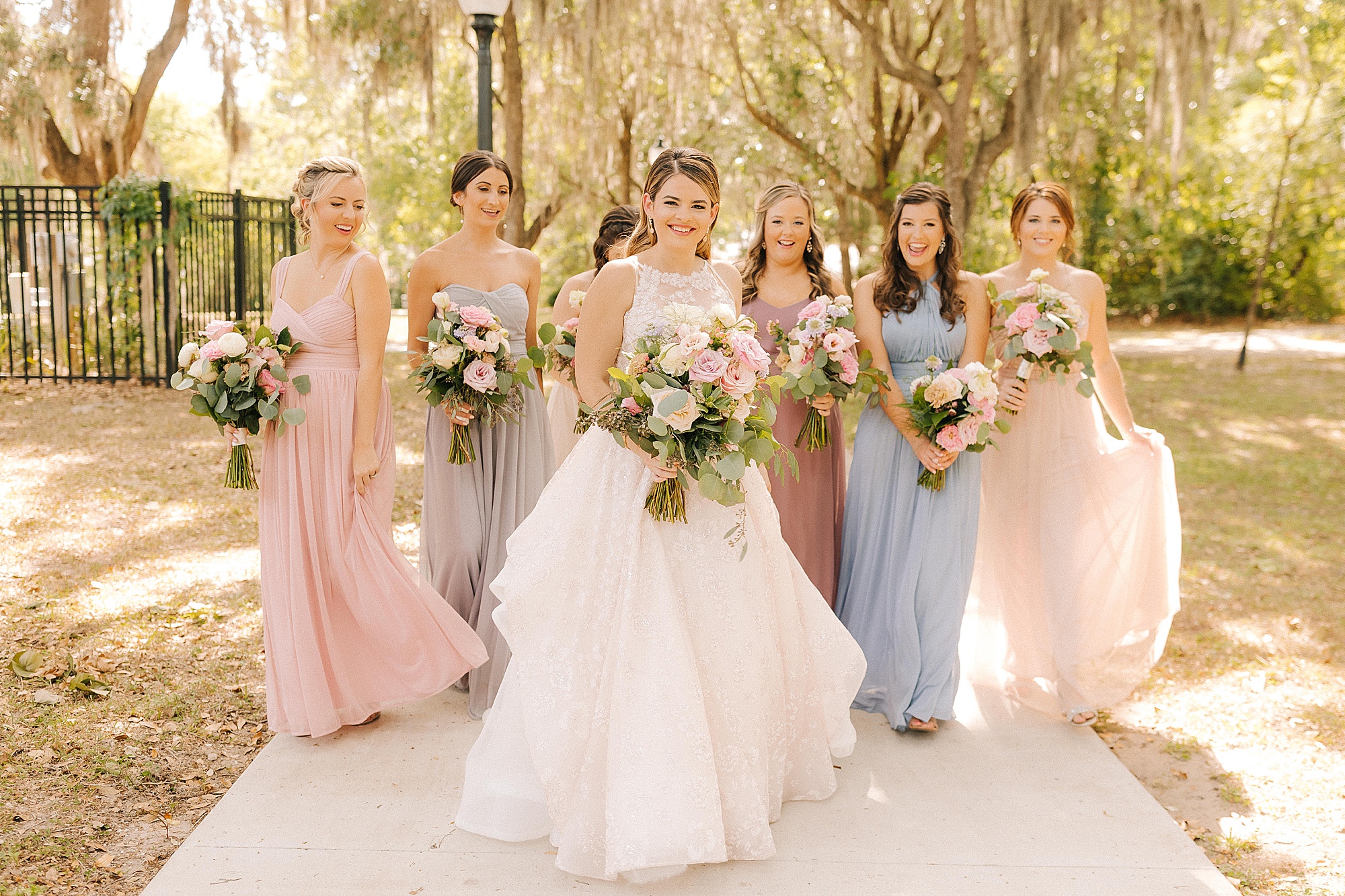 bride poses with bridesmaids in pink and blue gowns