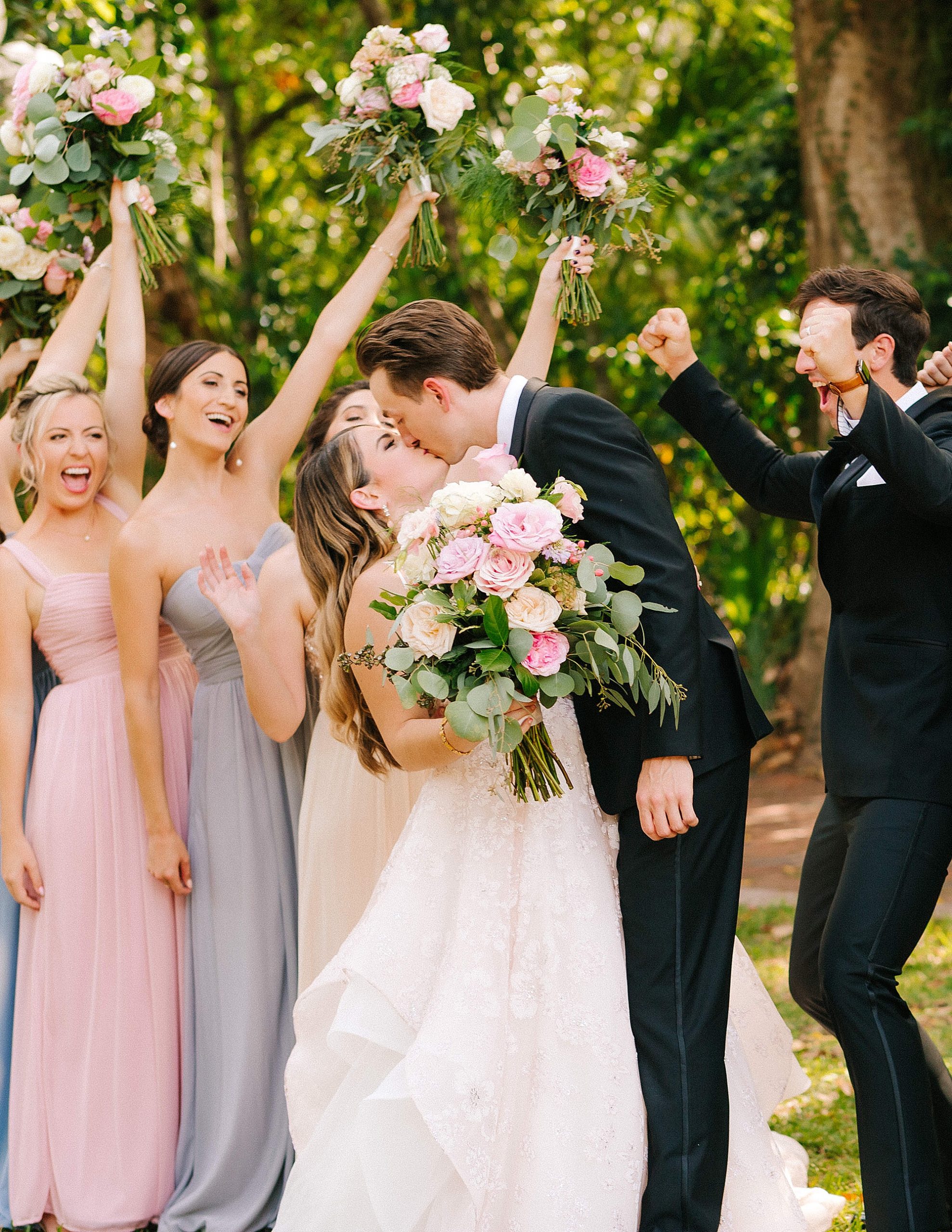 newlyweds kiss with wedding party cheering them on