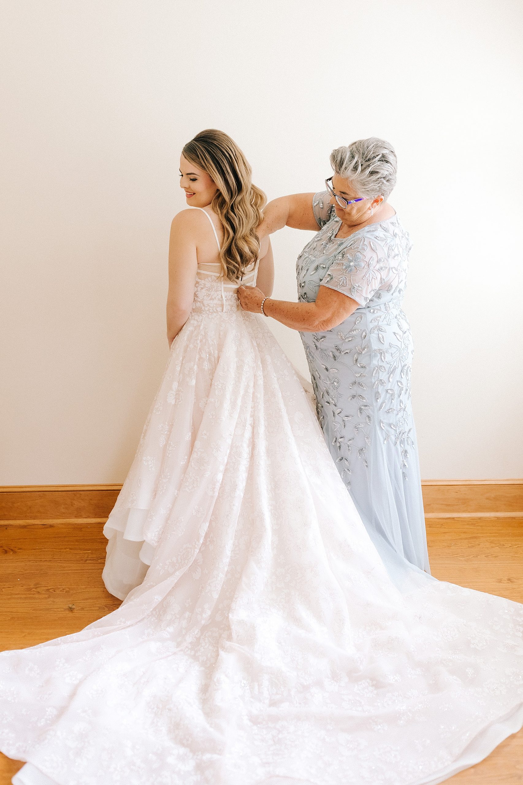 mother helps bride with gown on wedding day