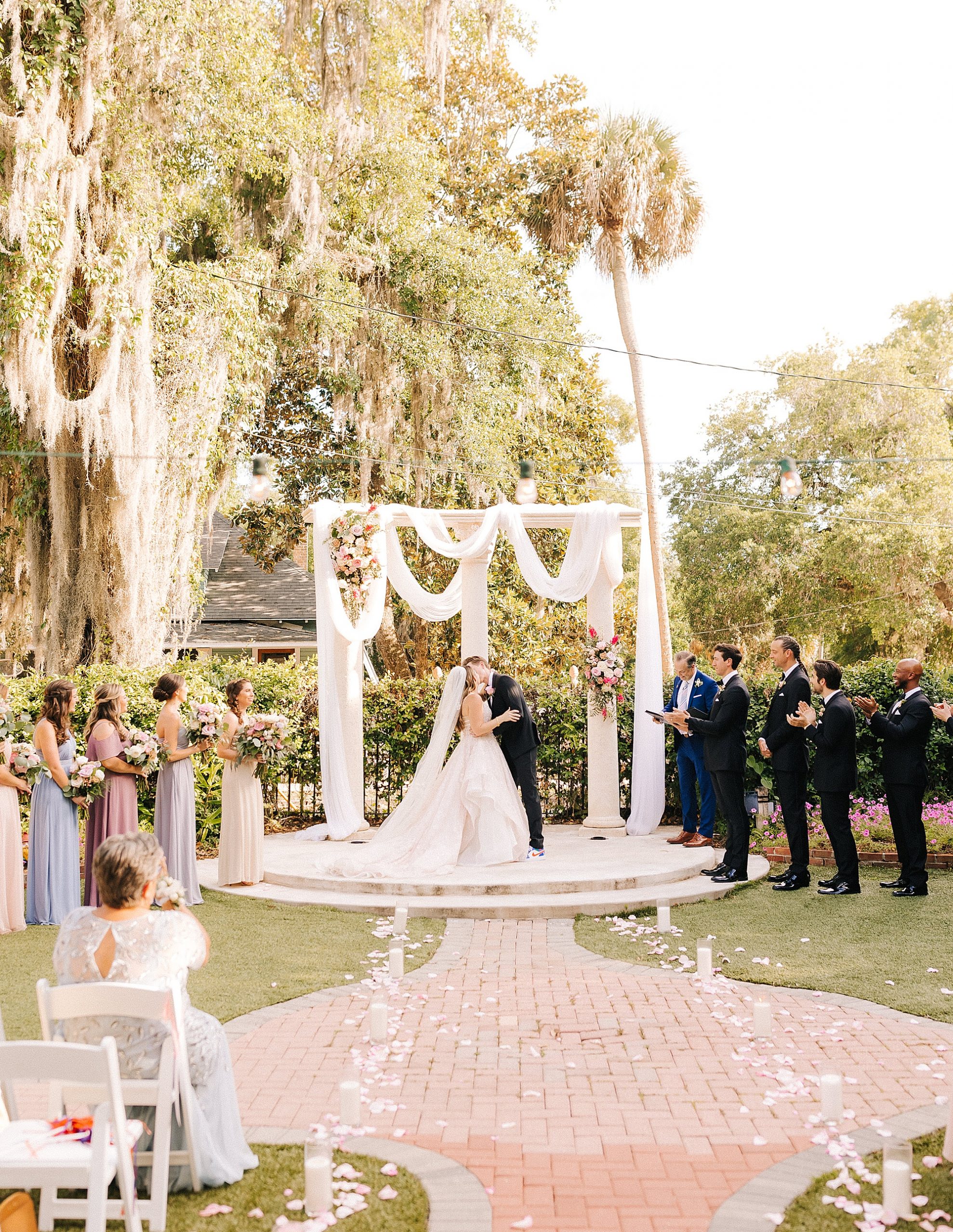 bride and groom kiss under arbor with draped white cloth