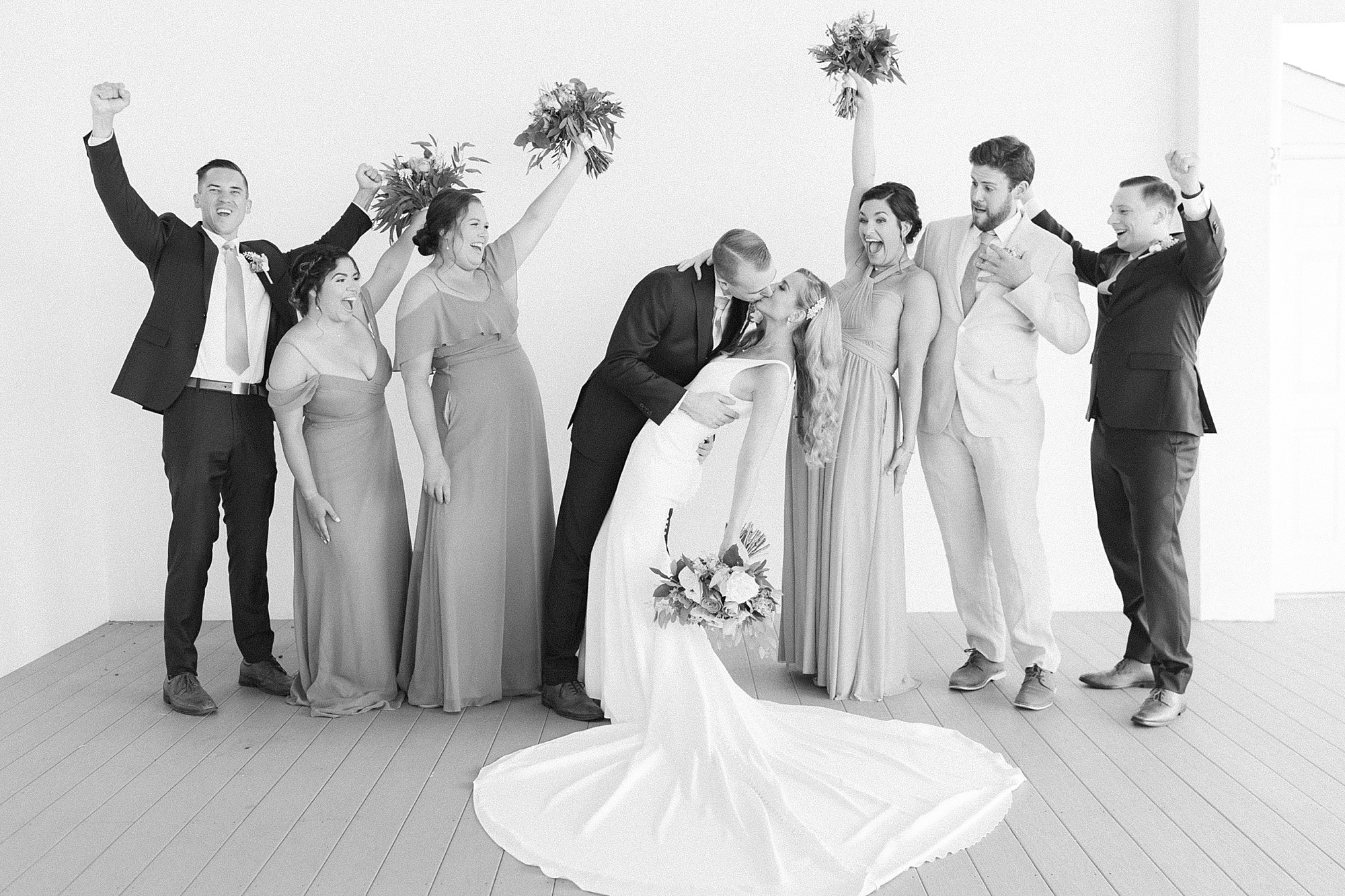 groom kisses bride while bridal party cheers