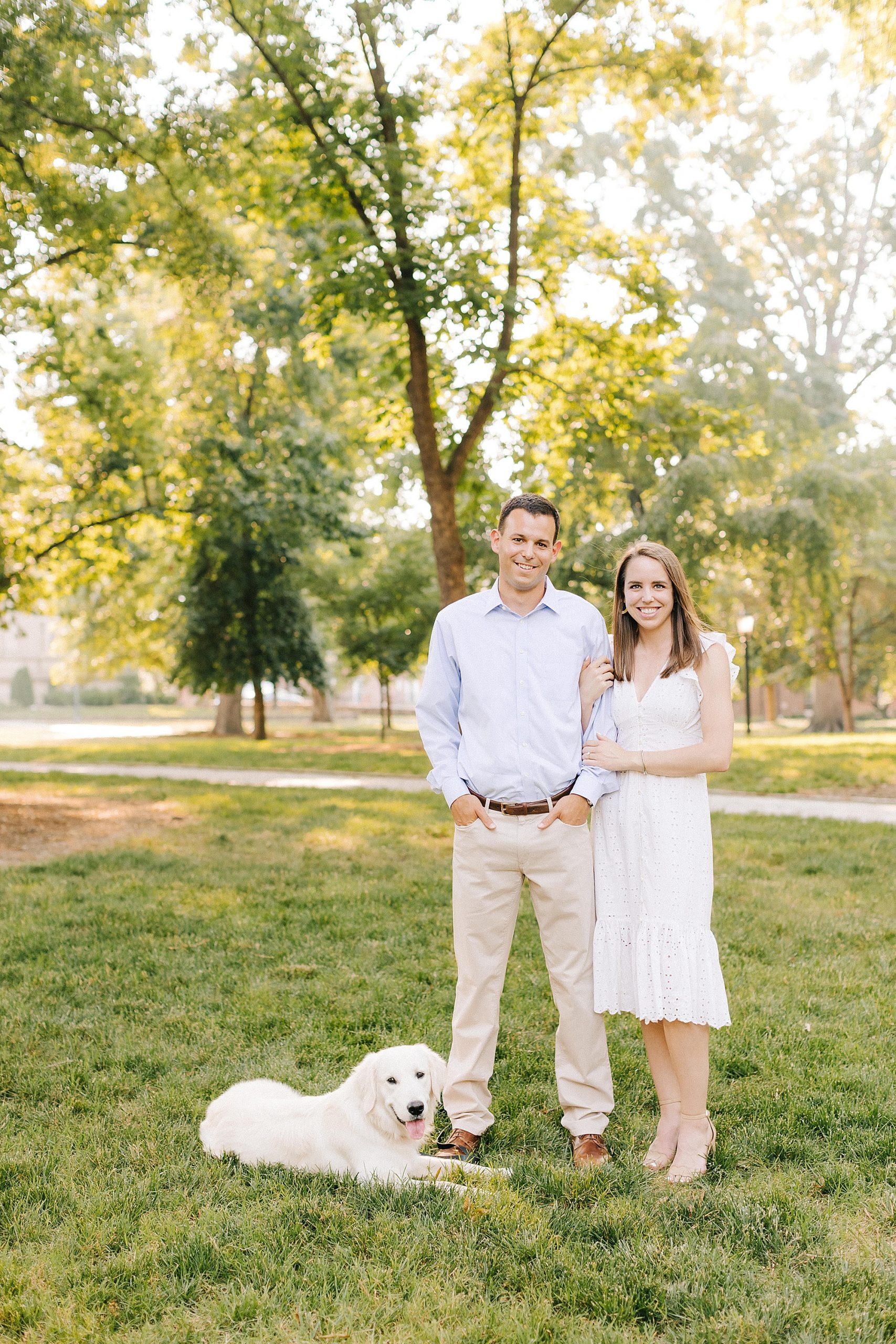 engaged couple poses with white dog in grass at UNC Chapel Hill