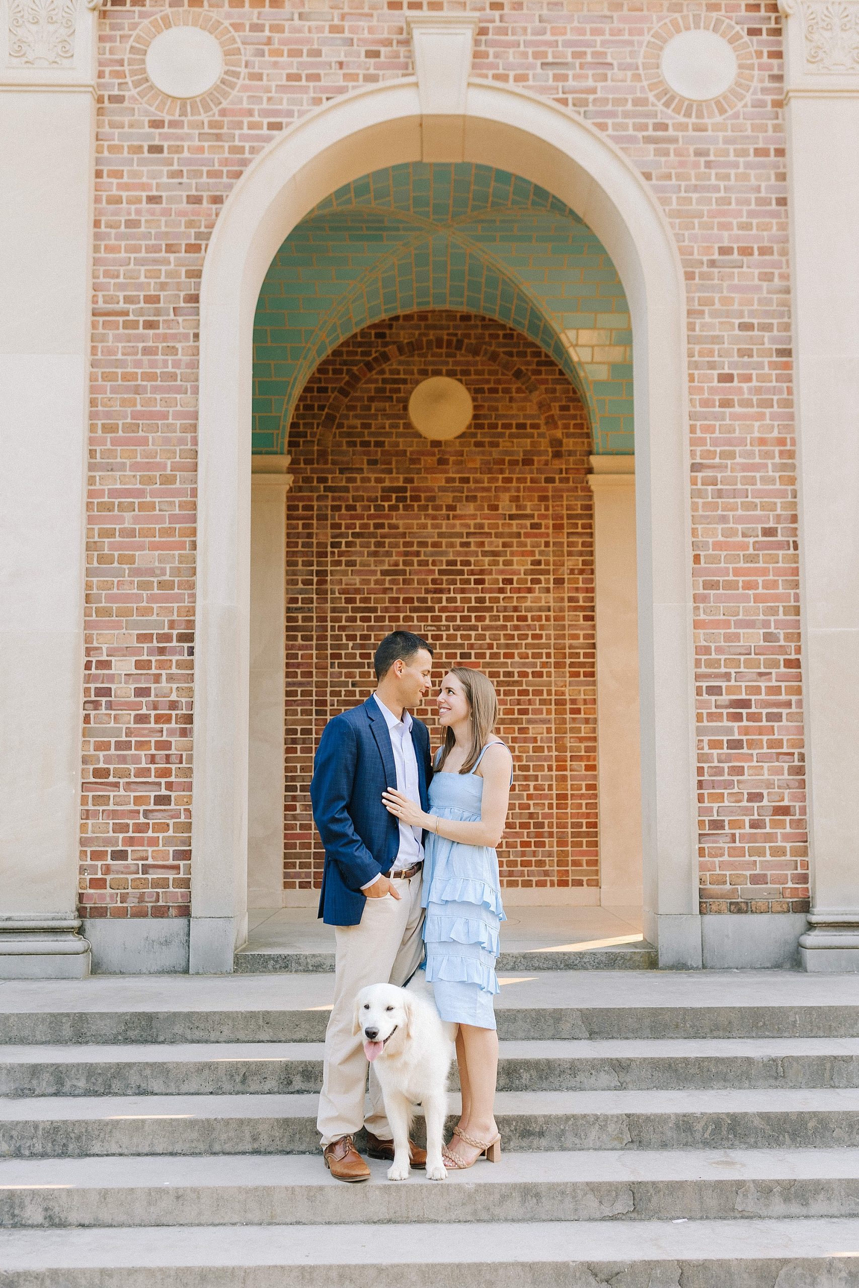 engaged couple poses on steps of building at UNC Chapel Hill with dog