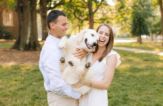 couple laughs holding their dog during UNC Chapel Hill Engagement Session